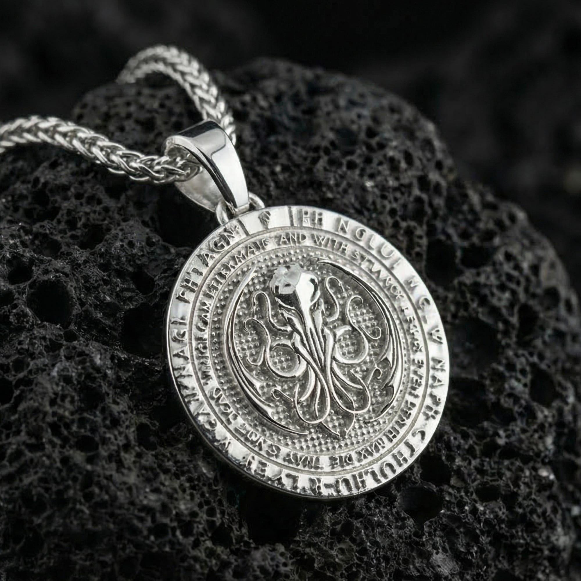 Polished silver Cthulhu sigil pendant displayed on volcanic stone background with intricate circular relief and arcane text