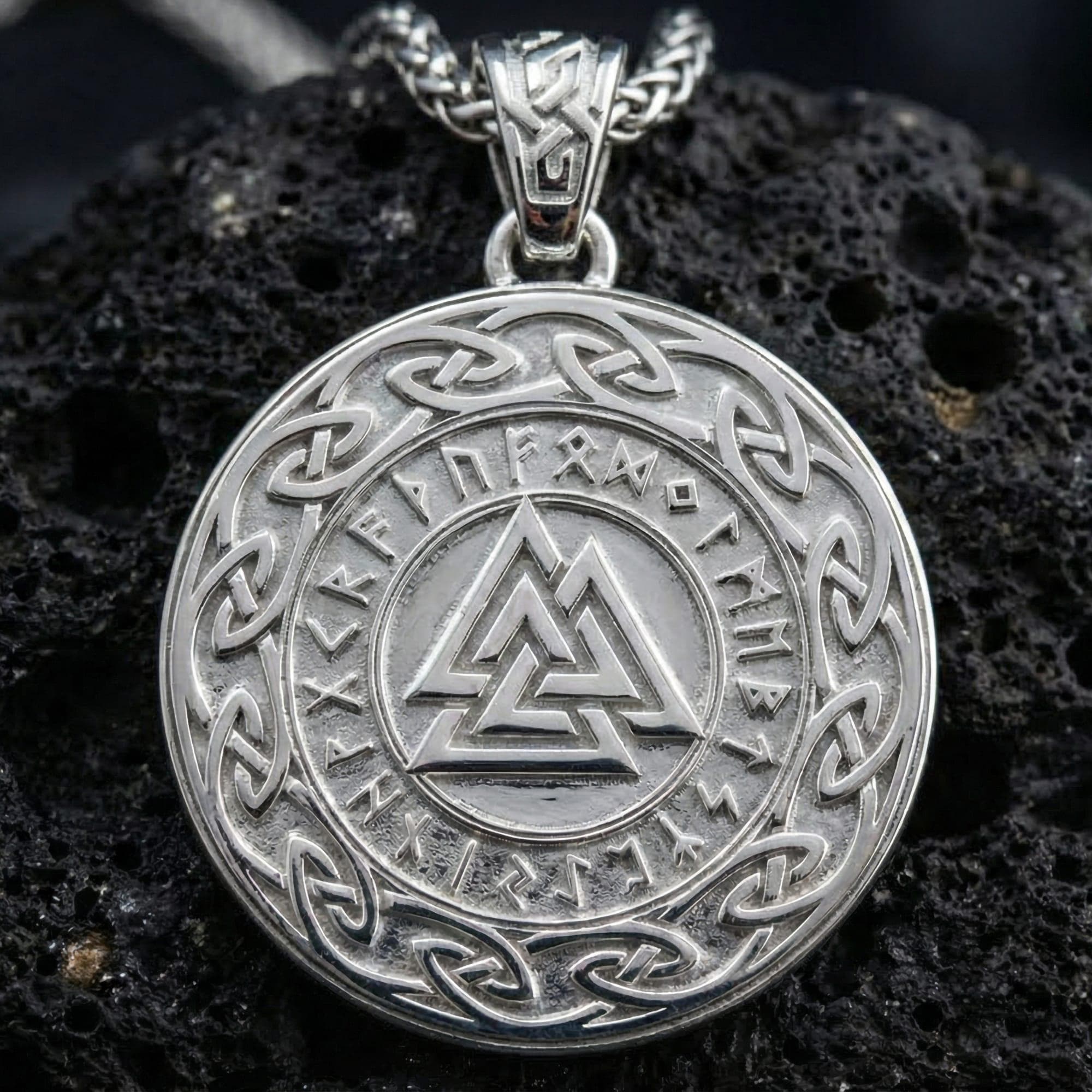 Polished silver Valknut Norse rune pendant displayed on volcanic stone background with sharp geometric relief and knotwork