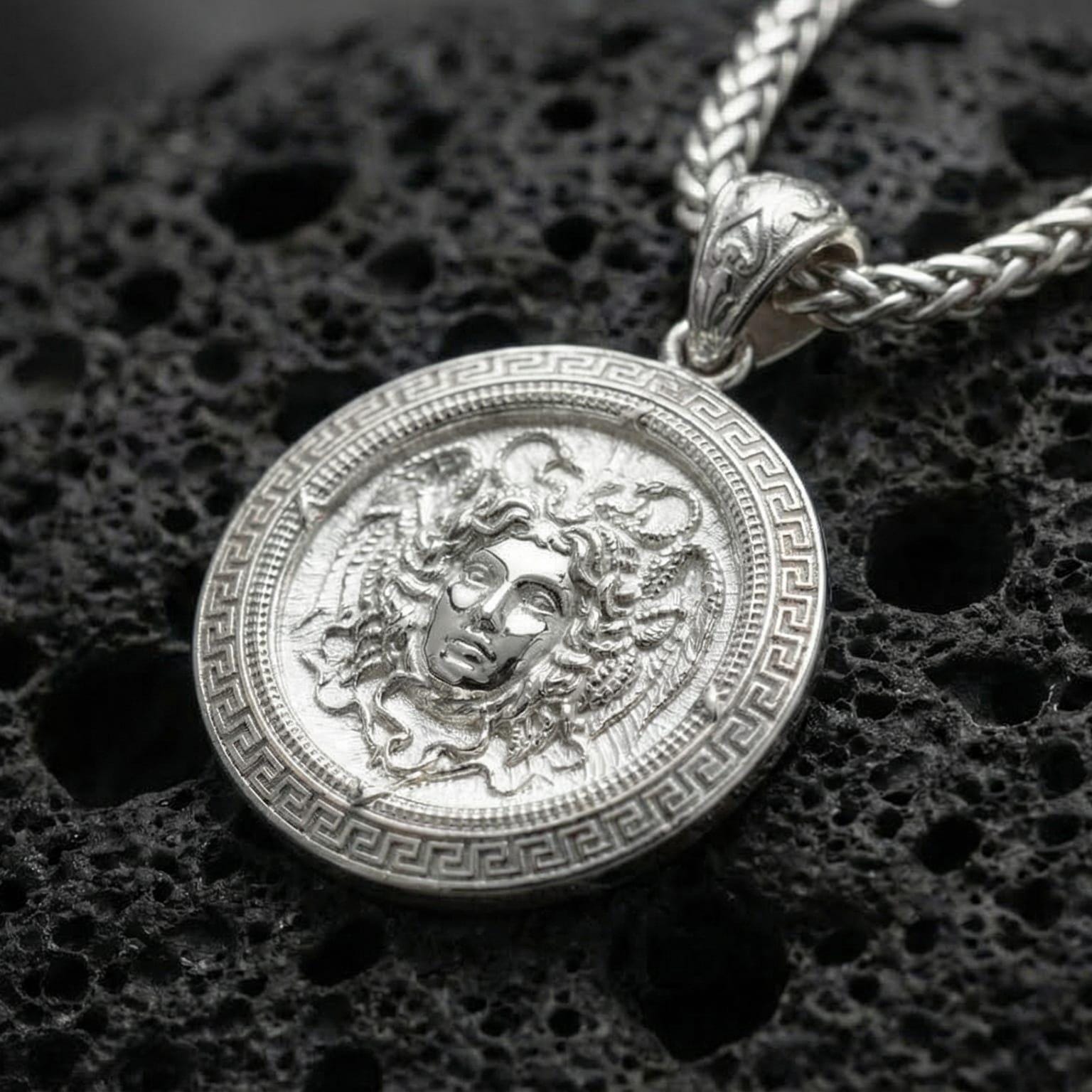 Polished silver Medusa Greek mythology pendant displayed on volcanic stone background highlighting detailed serpent hair engraving