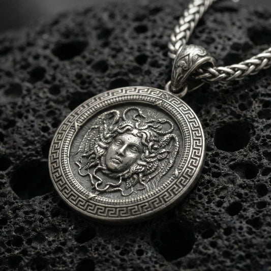 Oxidized Medusa pendant necklace photographed on volcanic rock with deep relief Gorgon face and Greek key border