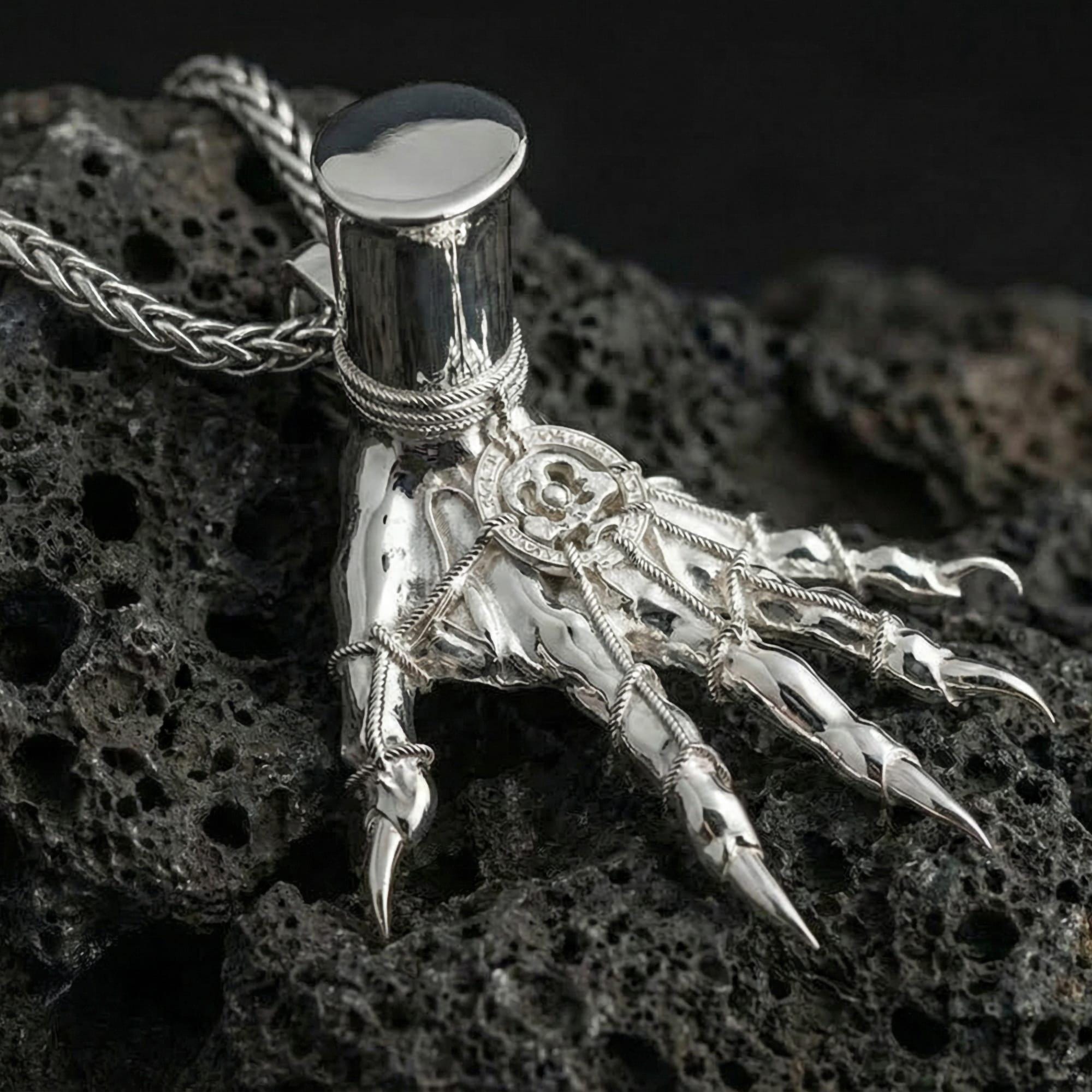 Polished silver Elden Ring inspired Hand of Maliketh pendant displayed on volcanic stone background highlighting sharp talon detail