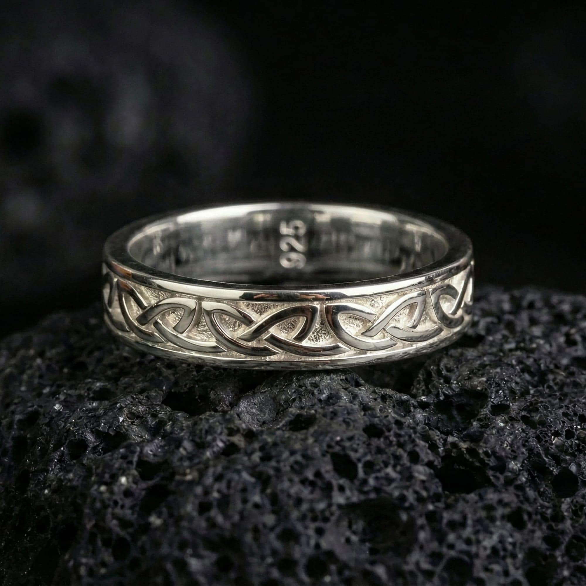 Polished silver Celtic knot band ring displayed on volcanic stone background highlighting smooth edges and intertwined design