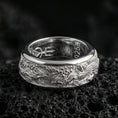 Load image into Gallery viewer, Polished silver phoenix spinner ring displayed on volcanic stone background emphasizing rotating band mechanism and detailed flame engraving
