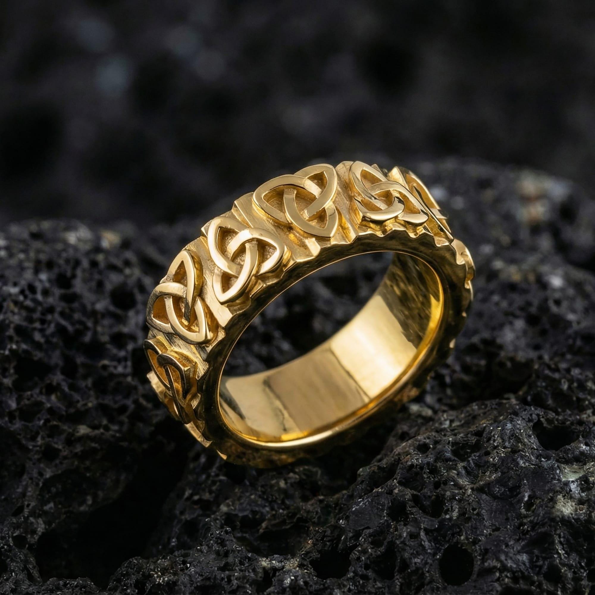 Gold Celtic trinity knot band ring displayed on volcanic rock as symbolic jewelry