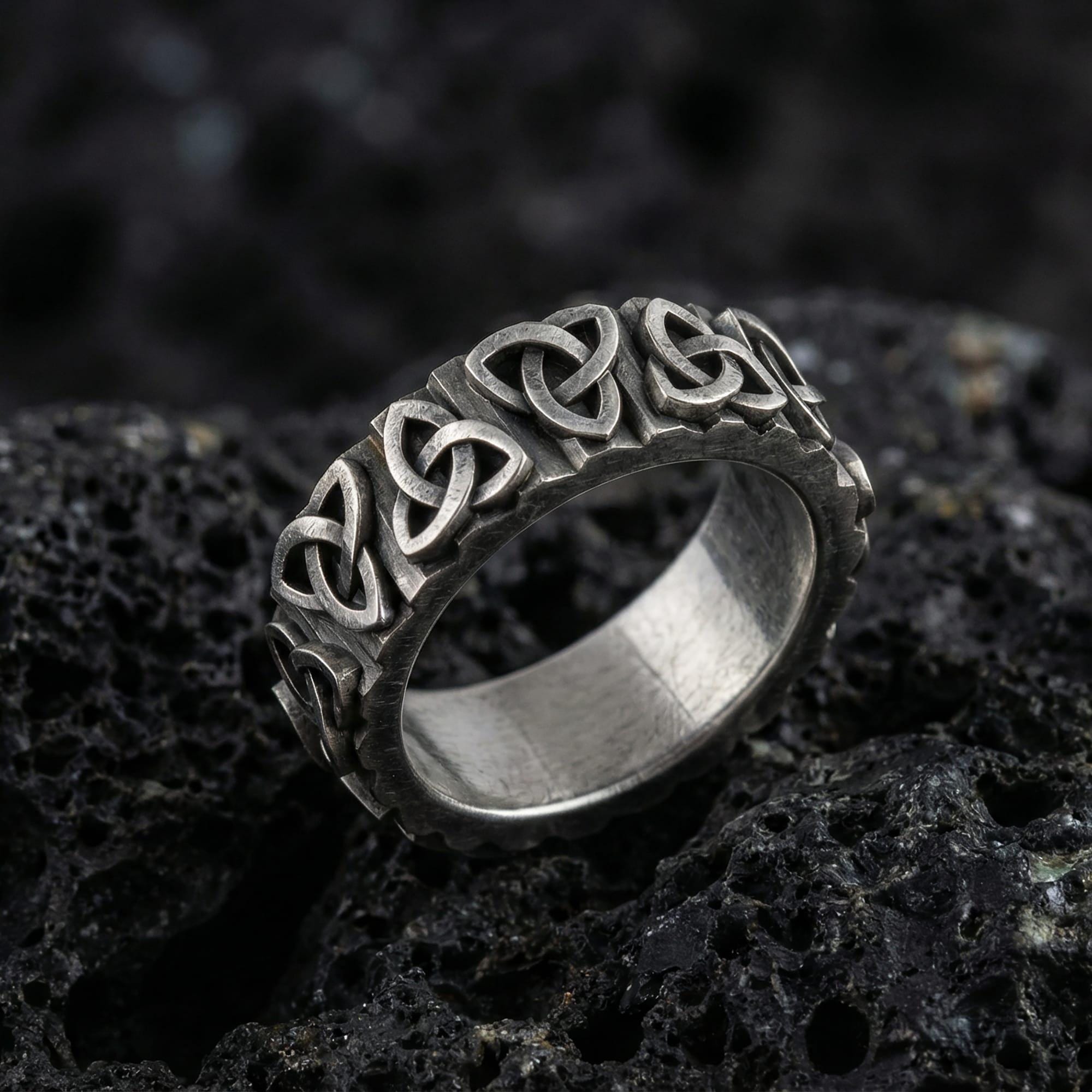 Oxidized sterling silver Celtic trinity knot band ring photographed on volcanic rock background