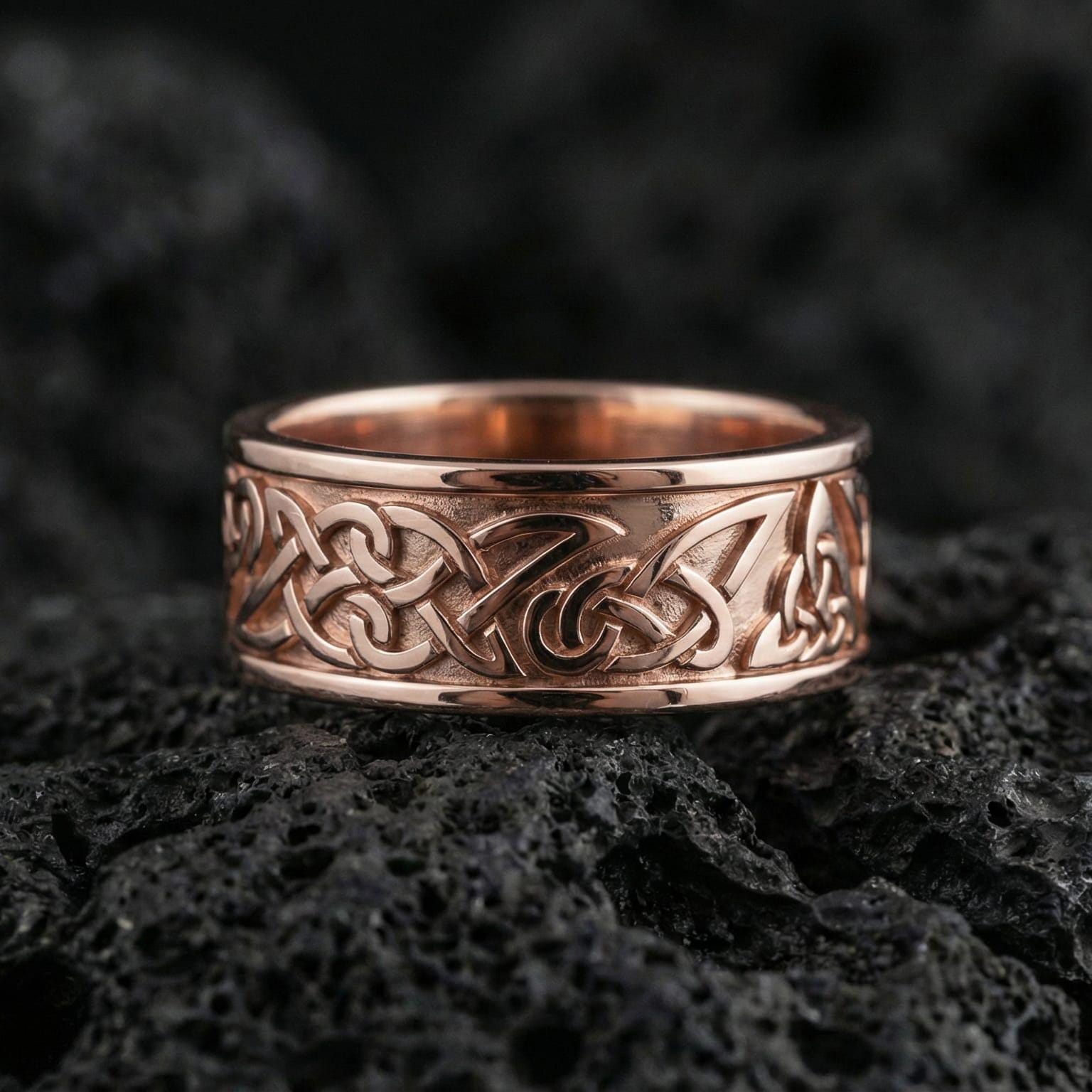 Rose gold plated Celtic knot ring presented on volcanic rock surface with warm metallic tone and intricate interwoven pattern detail