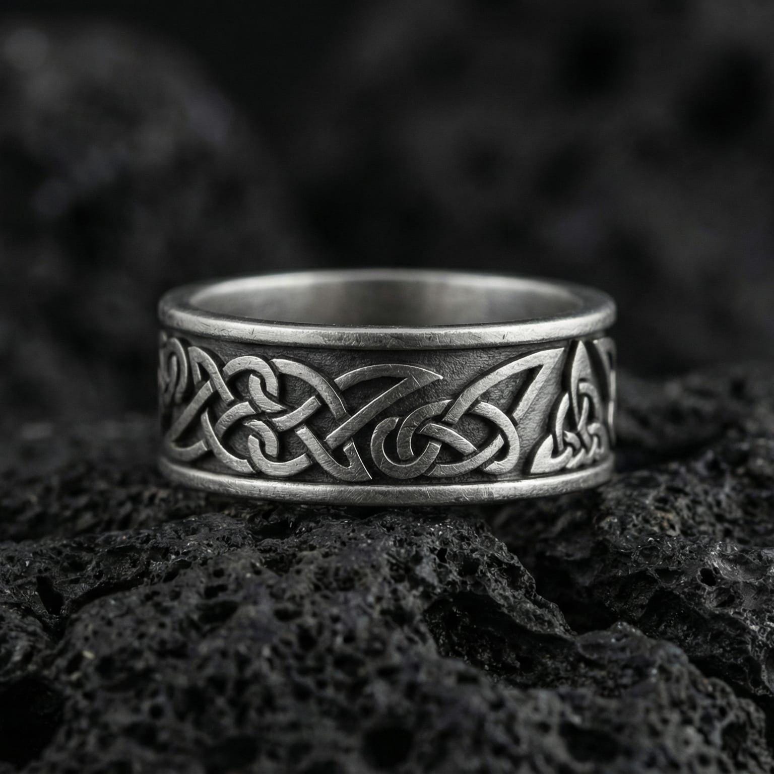 Oxidized Celtic knot band ring photographed on volcanic rock with interlaced Viking braid engraving and dark antique contrast
