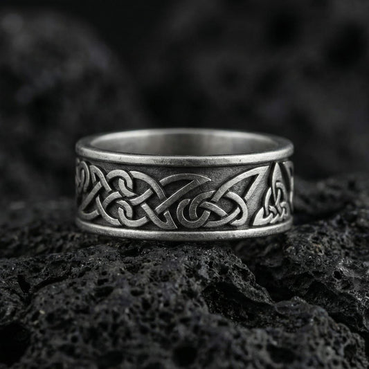 Oxidized Celtic knot band ring photographed on volcanic rock with interlaced Viking braid engraving and dark antique contrast