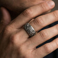 Load image into Gallery viewer, Oxidized sterling silver ornate cross band ring worn on a finger, lifestyle wear image showing bold sculpted depth and vintage-style contrast in natural light.
