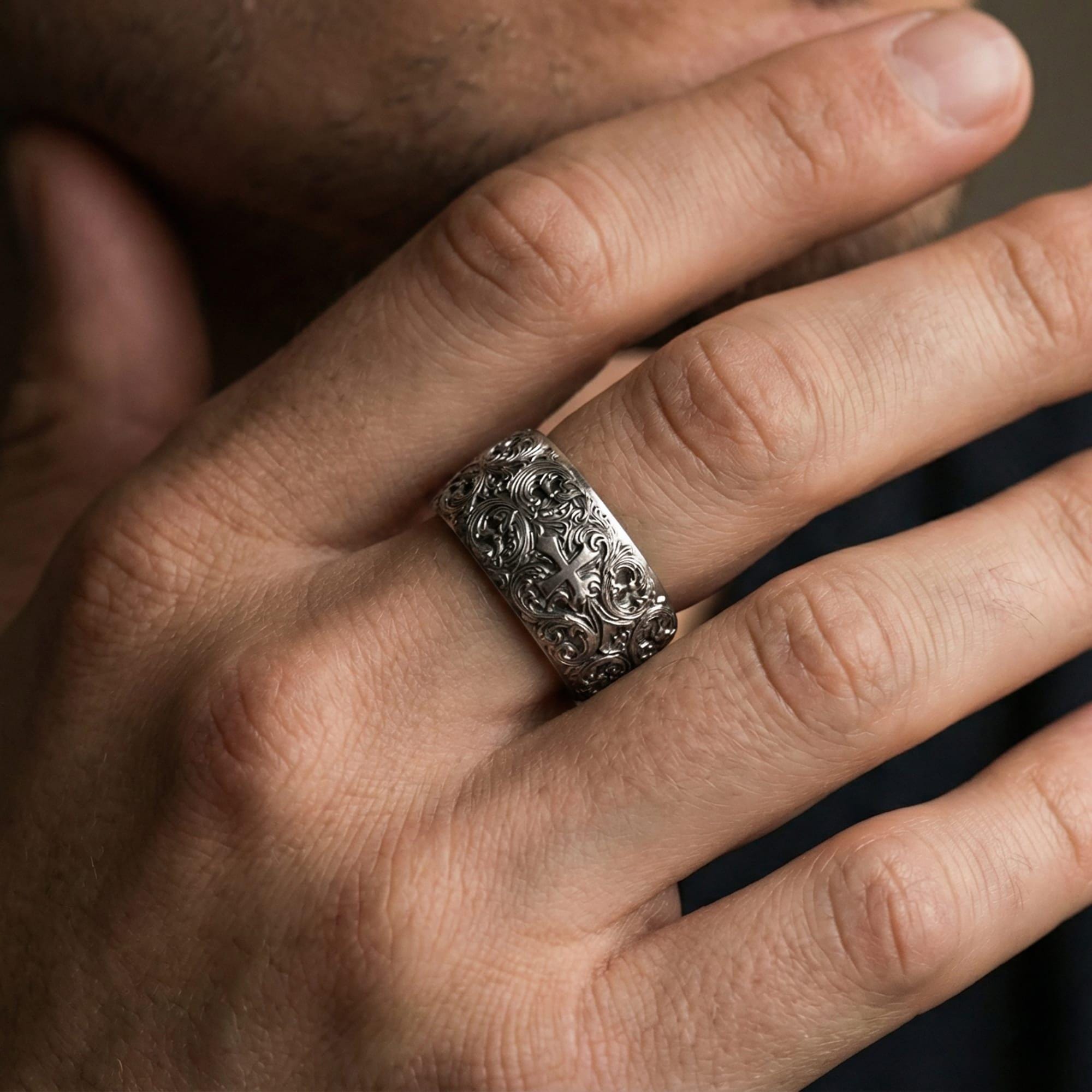Oxidized sterling silver ornate cross band ring worn on a finger, lifestyle wear image showing bold sculpted depth and vintage-style contrast in natural light.
