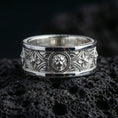 Load image into Gallery viewer, Polished silver lion emblem band ring displayed on volcanic stone background highlighting symmetrical scrollwork lines and bold masculine silhouette
