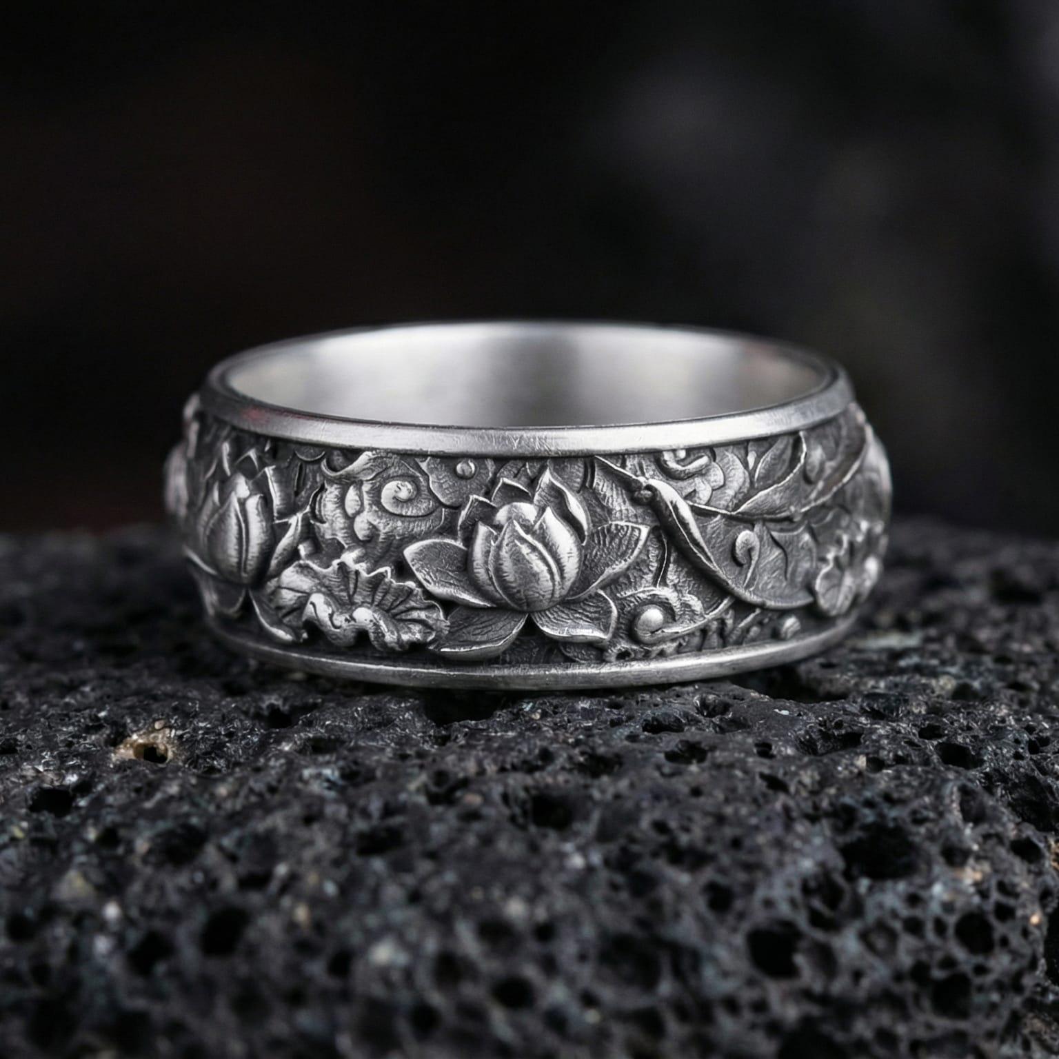 Oxidized lotus flower engraved band ring photographed on volcanic rock with detailed floral relief and artisan botanical texture