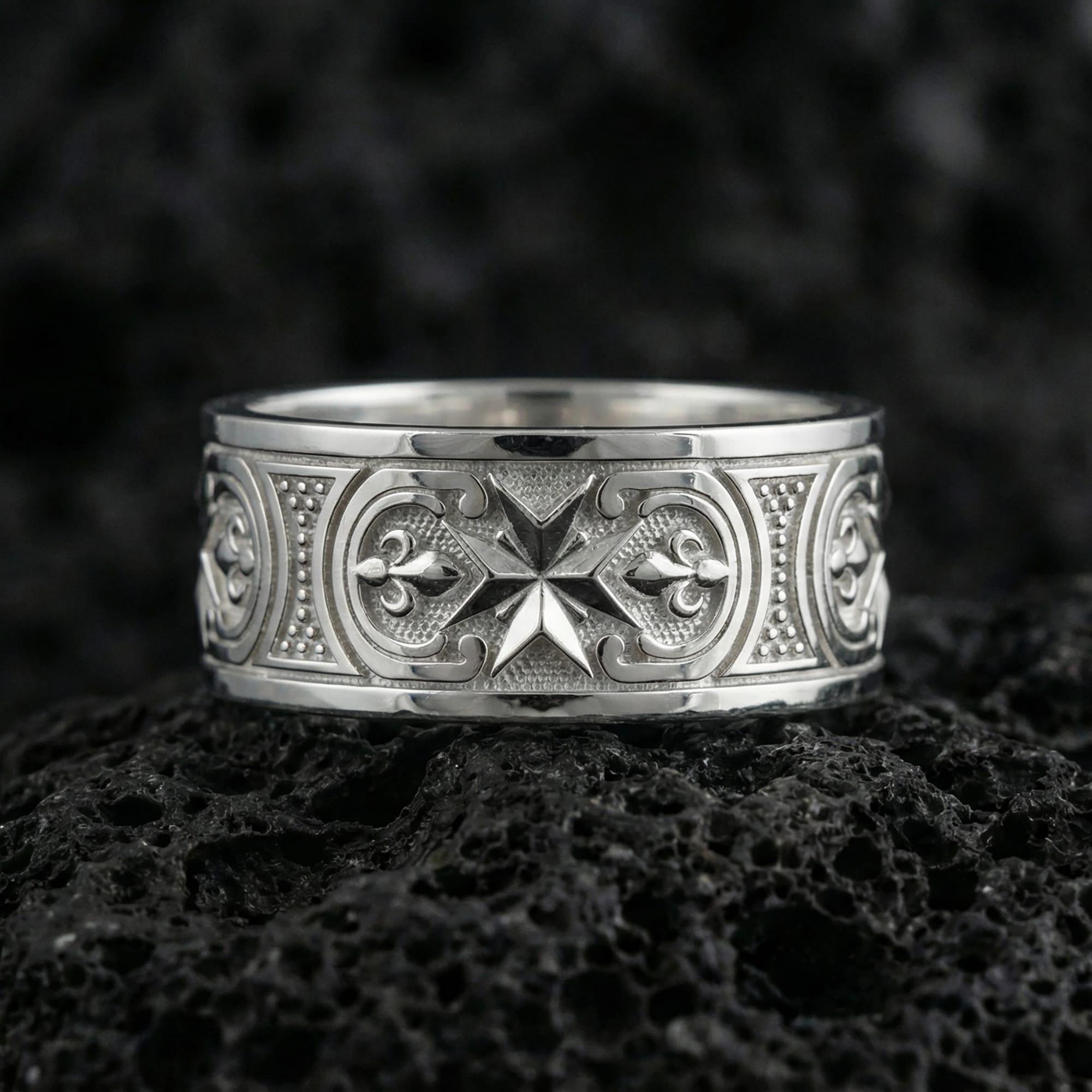 Polished silver crusader Maltese cross ring displayed on volcanic stone background, highlighting raised medieval cross motif with ornamental border engraving