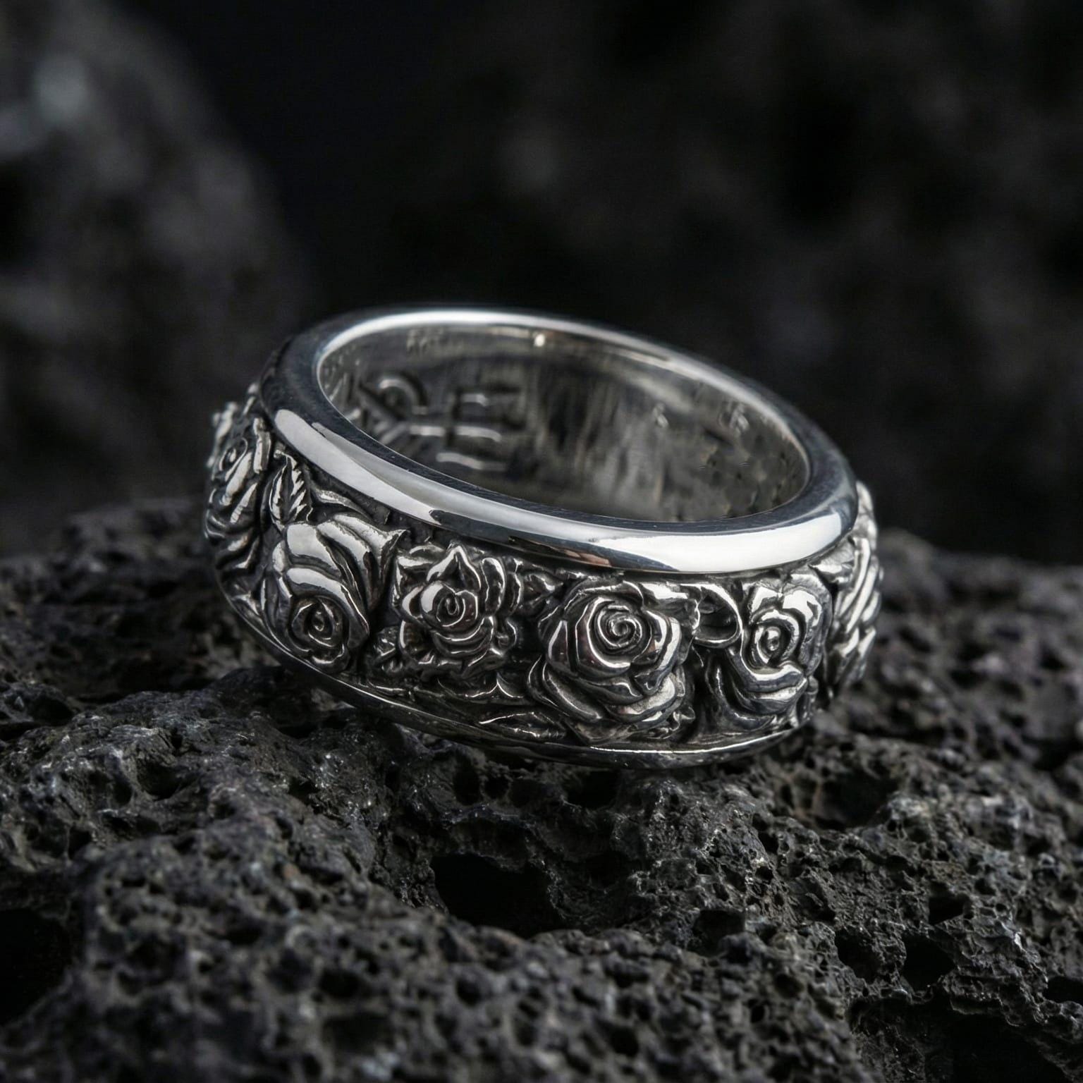 Polished silver rose spinner ring displayed on volcanic stone background highlighting crisp engraved roses, smooth edges, and clean reflective finish