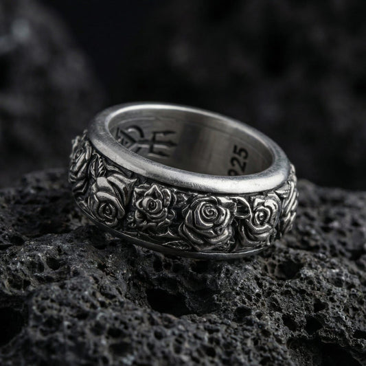 Oxidized spinning rose band ring photographed on volcanic rock showcasing deep floral relief, antique patina, and fidget-friendly rotating design