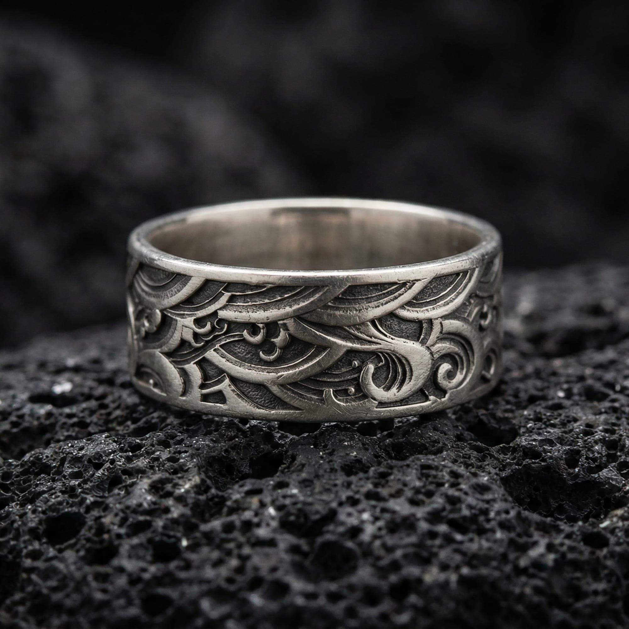 Oxidized sterling silver wave pattern band ring photographed on volcanic rock, featuring deep engraved swirls and vintage geometric texture