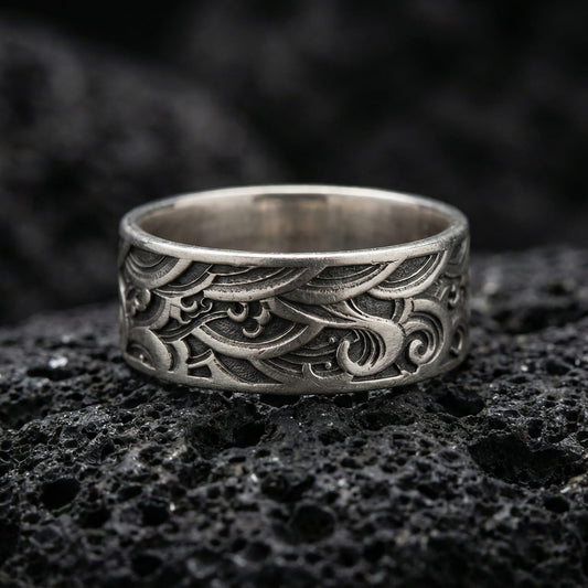 Oxidized sterling silver wave pattern band ring photographed on volcanic rock, featuring deep engraved swirls and vintage geometric texture