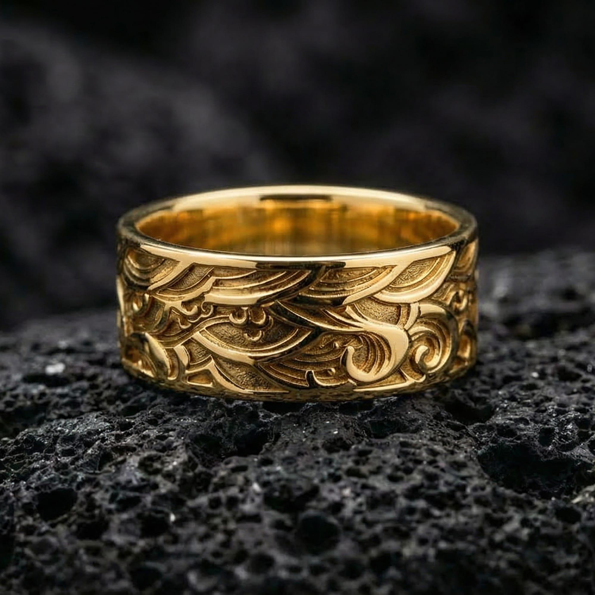 Gold plated wave motif sterling silver band ring showcased on volcanic rock with bold ocean-inspired engraving and premium statement finish