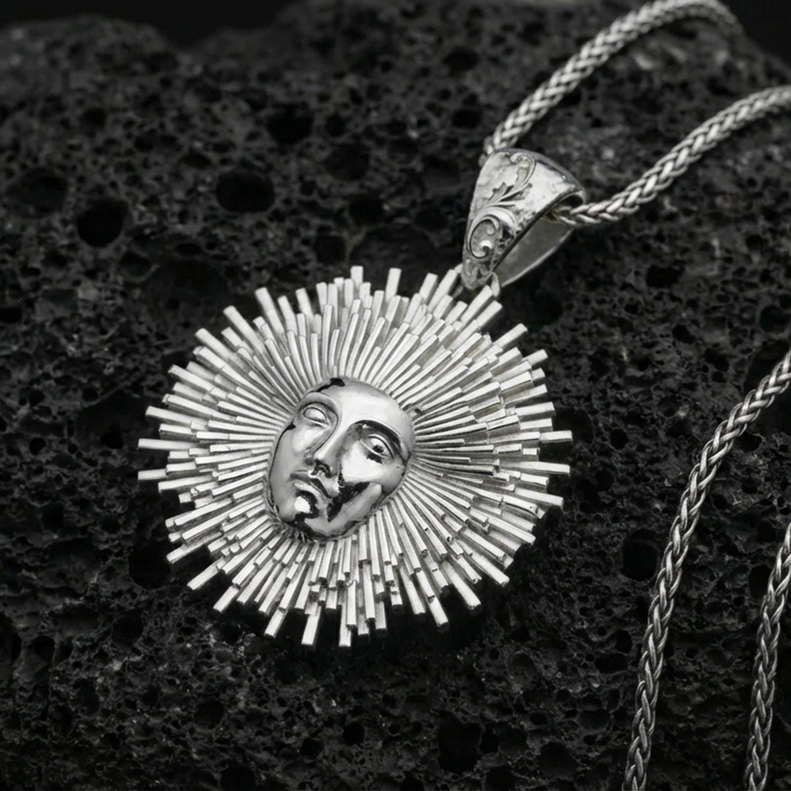 Polished silver Helios pendant necklace on porous volcanic stone, detailed sun god face with sharp sunburst rays