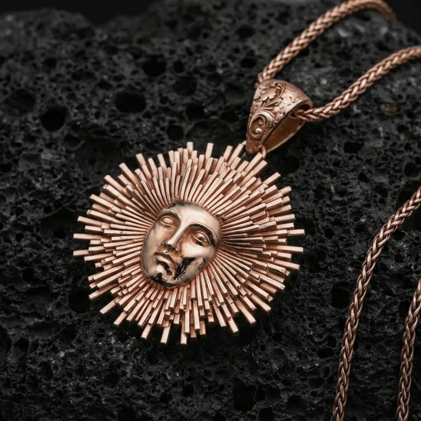 Rose gold plated Helios pendant necklace on dark volcanic stone, sunburst rays around Helios face with bail