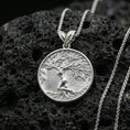 Load image into Gallery viewer, Polished silver Yggdrasil pendant necklace on porous volcanic stone, detailed tree branches and roots in round frame
