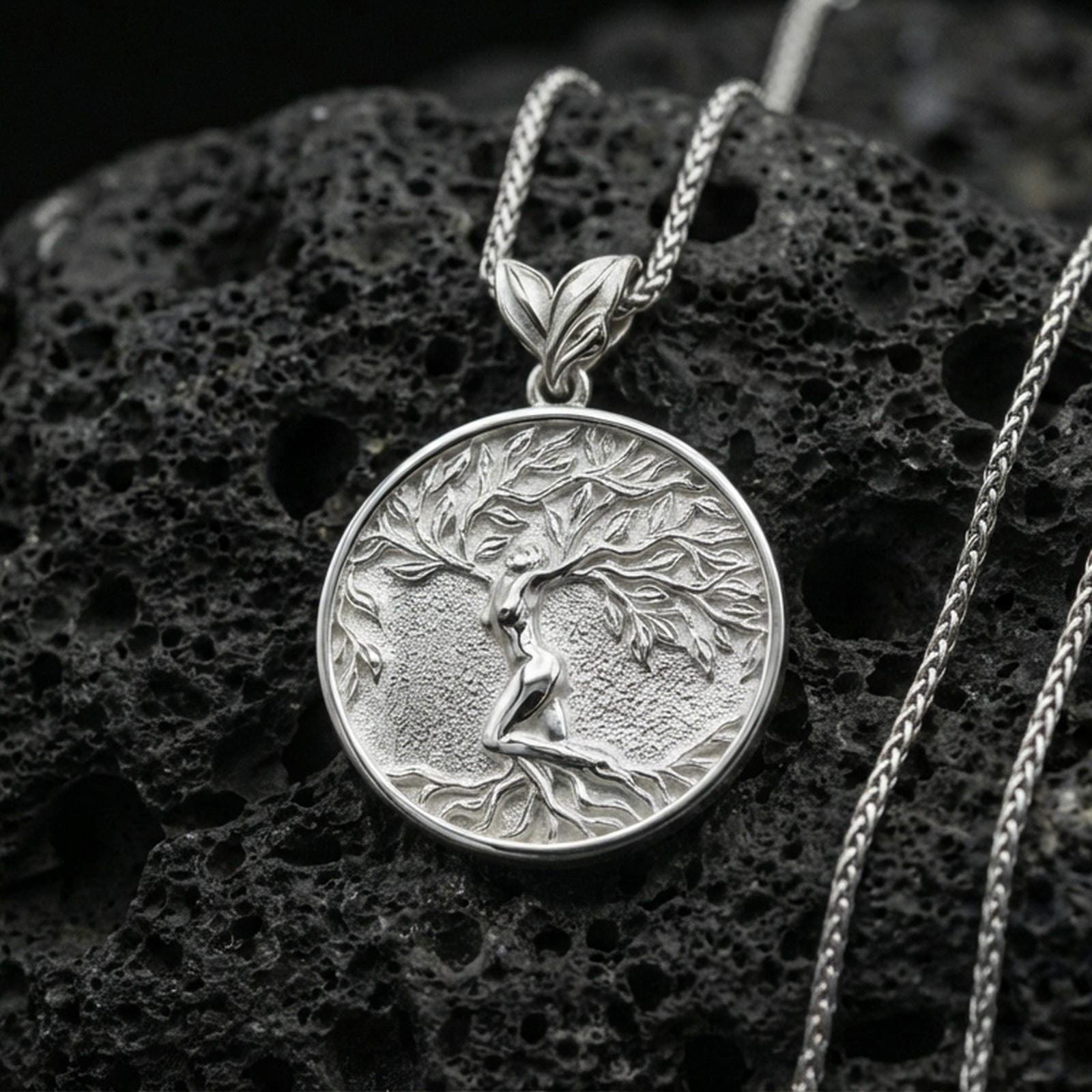Polished silver Yggdrasil pendant necklace on porous volcanic stone, detailed tree branches and roots in round frame
