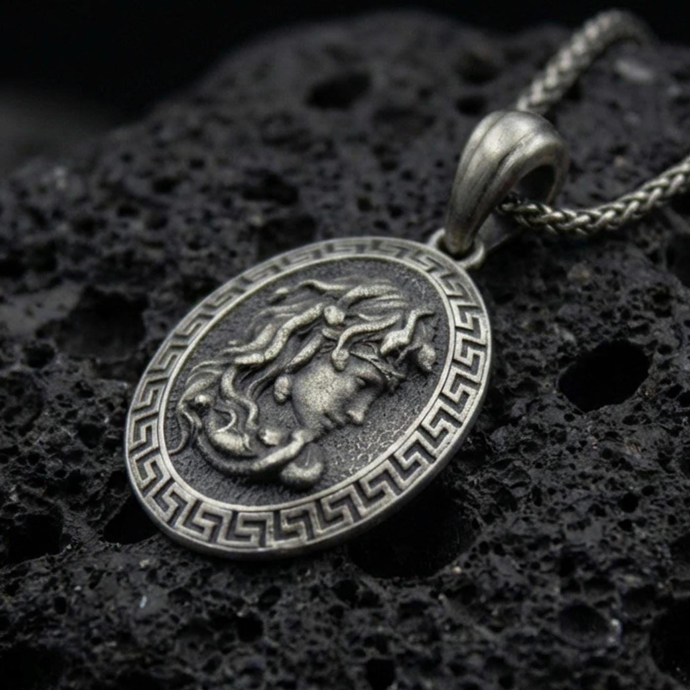 Oxidized 925 sterling silver Medusa coin pendant on volcanic rock, Greek key border medallion with raised goddess profile relief
