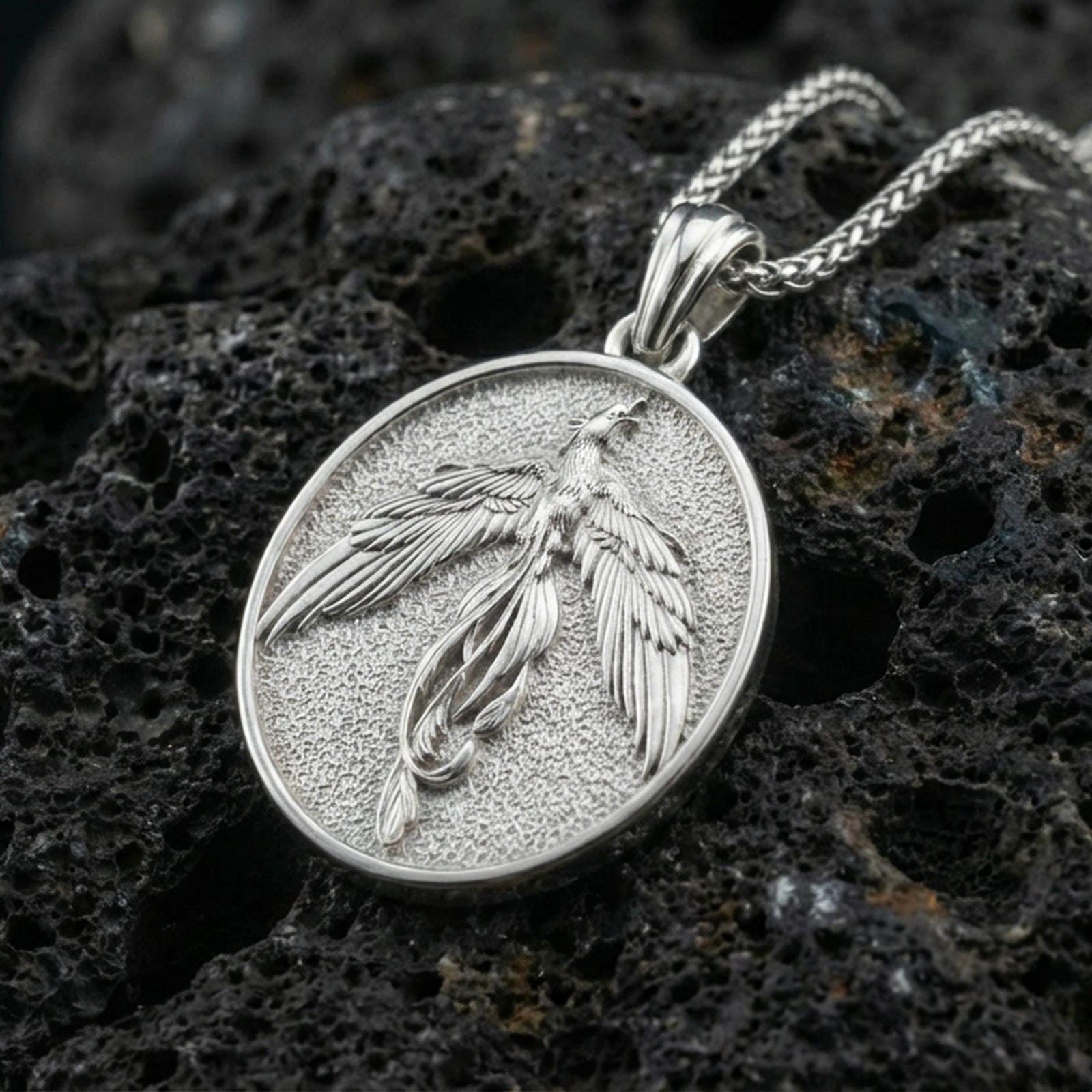 Polished silver phoenix medallion necklace on porous volcanic stone, flying bird pendant with crisp feather detailing