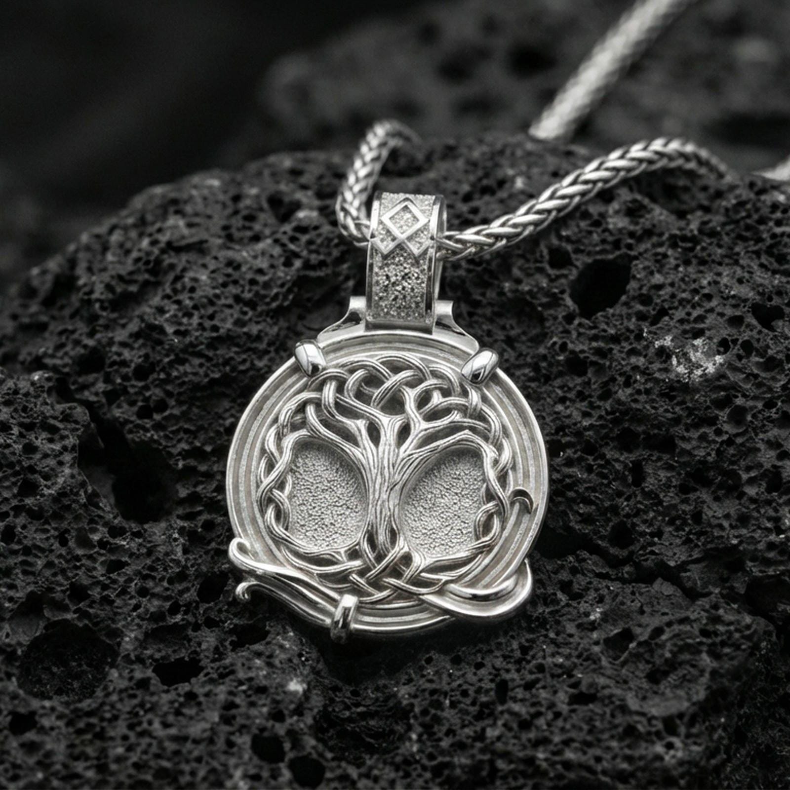 Polished silver yggdrasil pendant on porous volcanic stone, detailed tree of life relief with celtic knot border