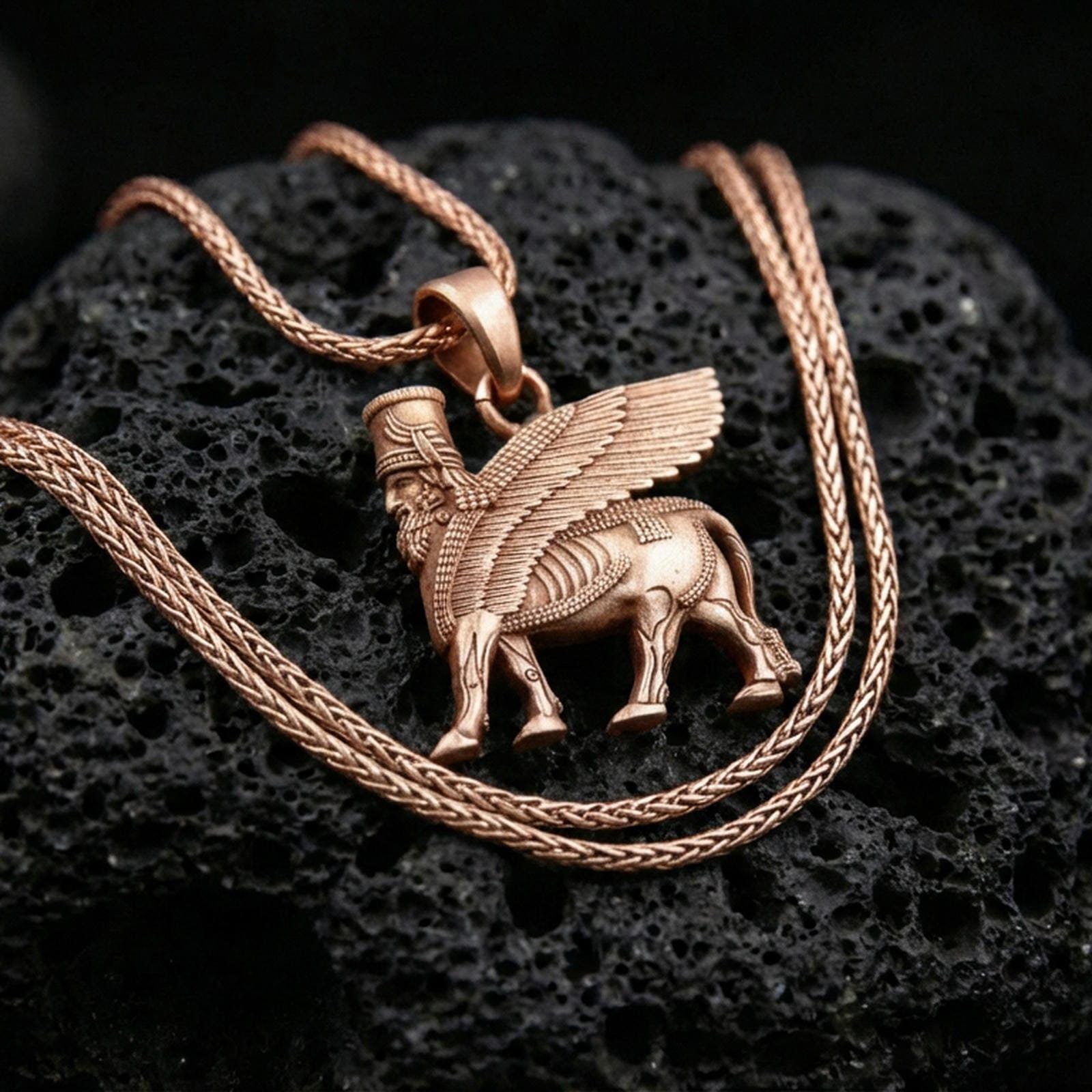 Rose gold plated lamassu necklace on dark volcanic stone, ancient Mesopotamian guardian spirit pendant with sculpted wings