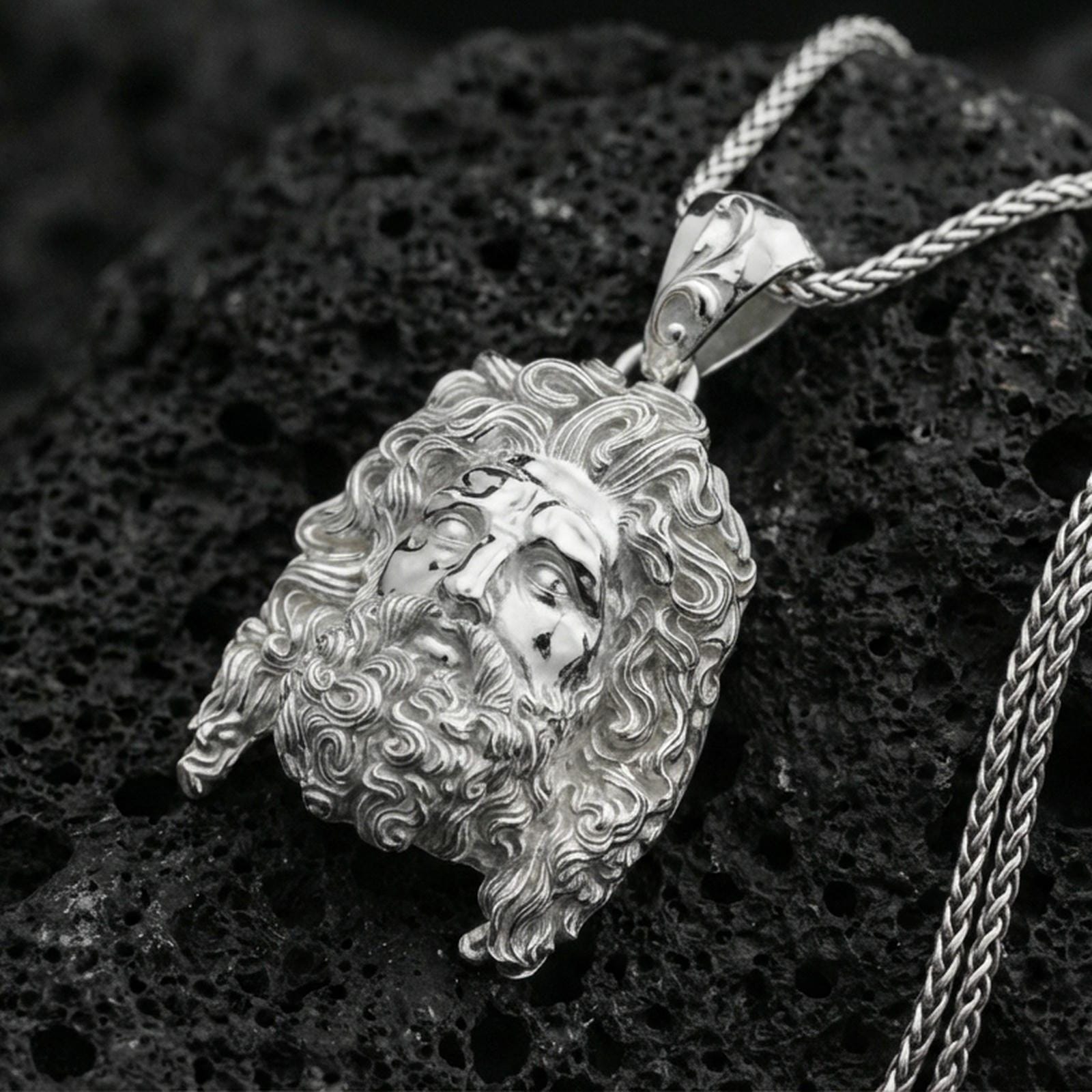 Polished silver deity head pendant on volcanic rock, high-contrast texture background, close-up craftsmanship detail