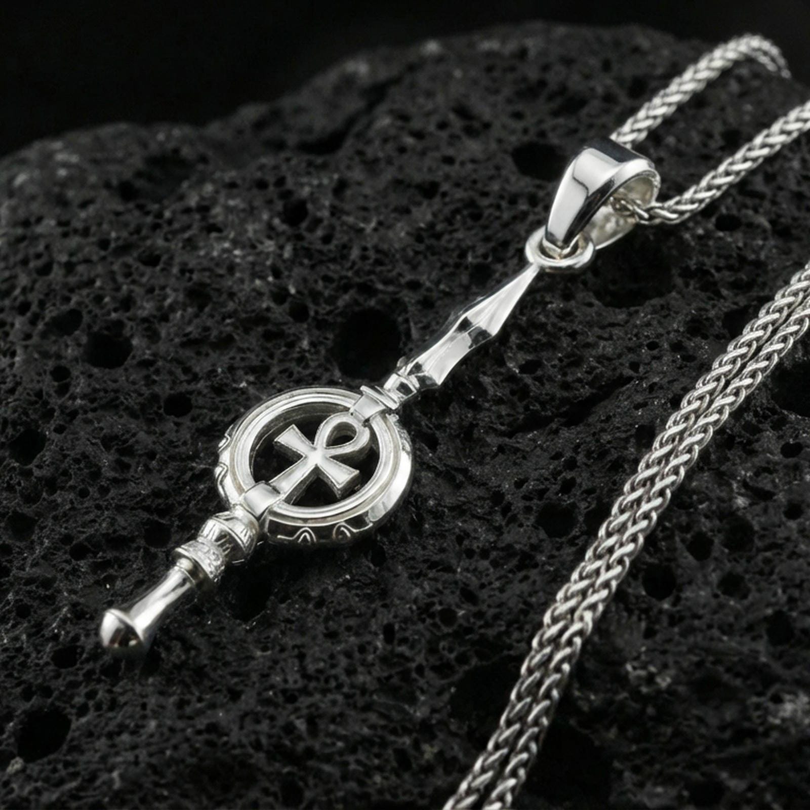 Polished silver ankh spear necklace on volcanic rock, clean reflective finish and sharp geometric lines, close-up