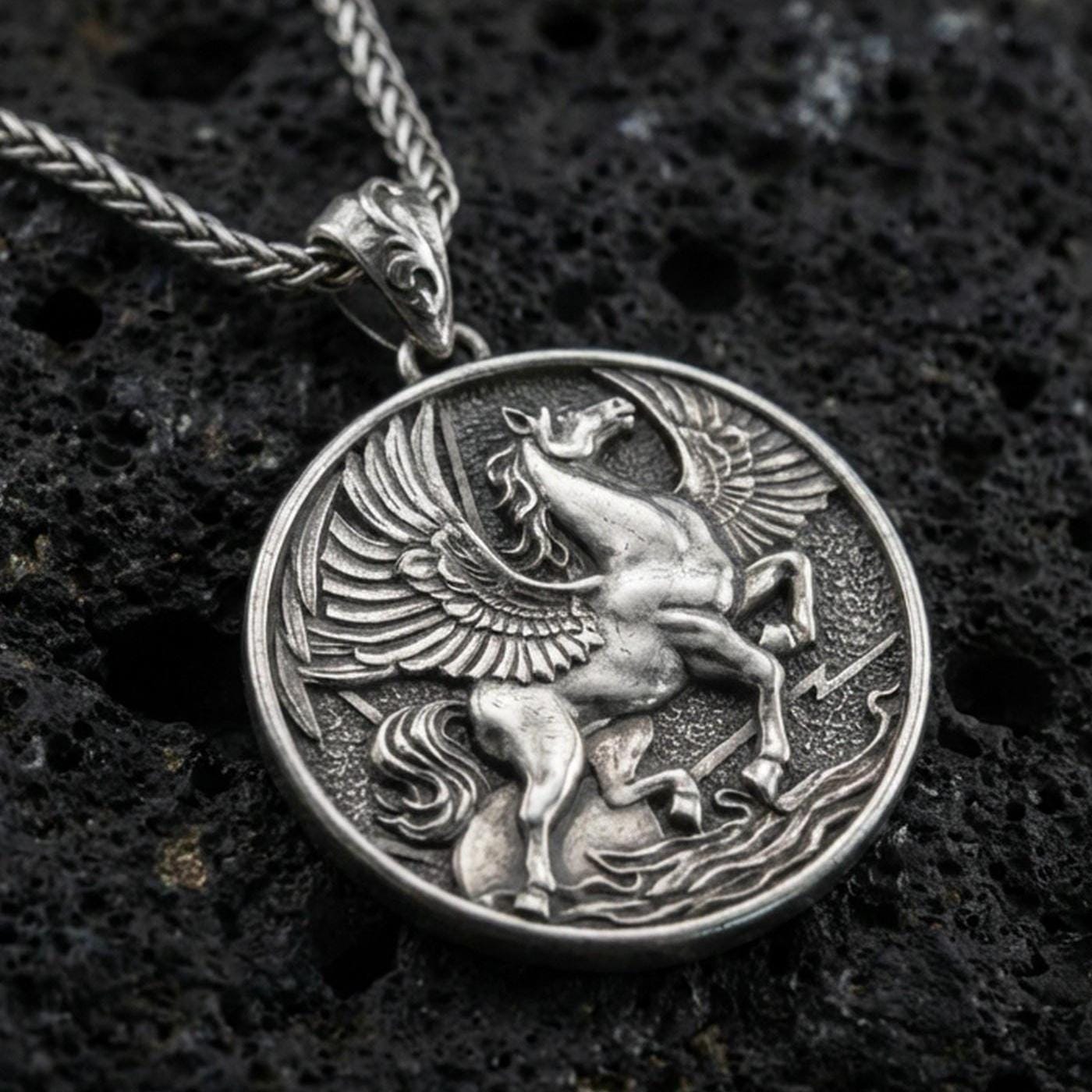 Oxidized sterling silver winged Pegasus medallion pendant on volcanic rock, high-relief flying horse design, macro shot
