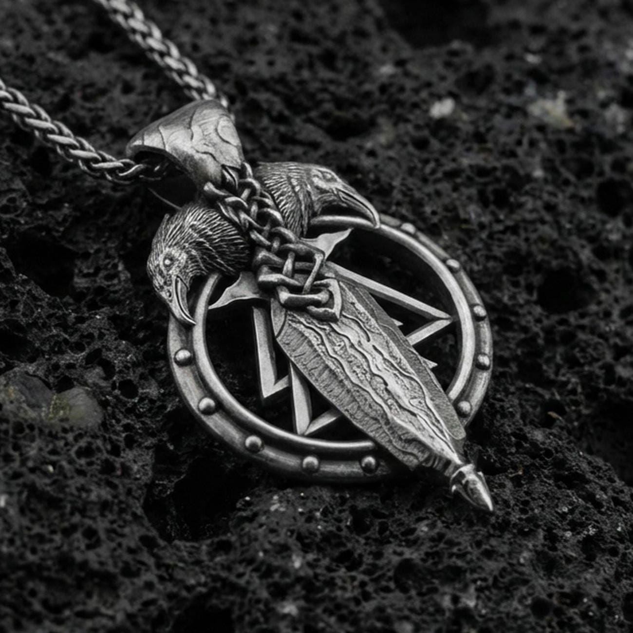 Oxidized sterling silver Odin’s spear and raven pendant on volcanic rock, Norse Viking talisman design, macro shot