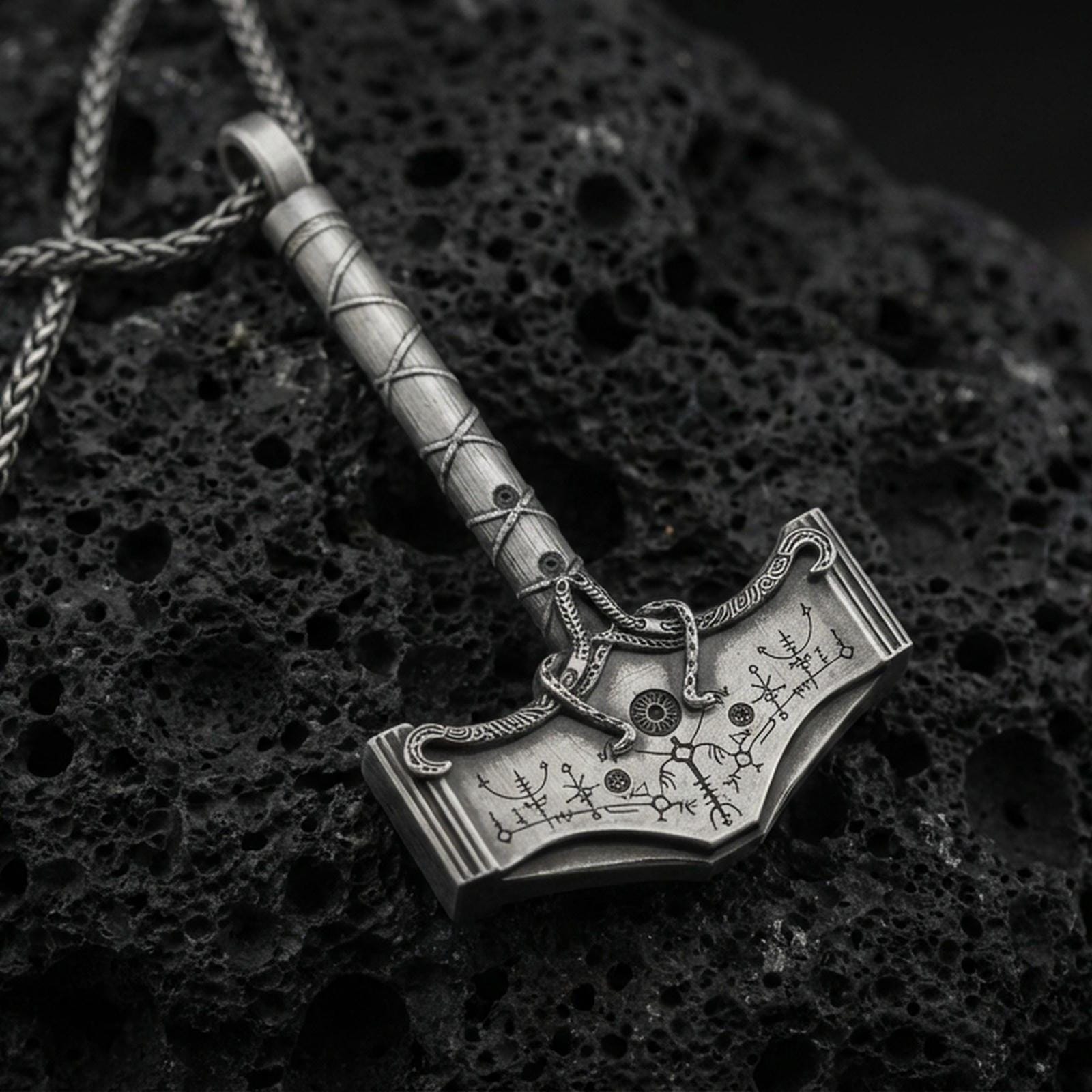 Oxidized sterling silver Mjolnir Thor hammer pendant on volcanic rock, engraved Nordic runes and knotwork, macro studio shot