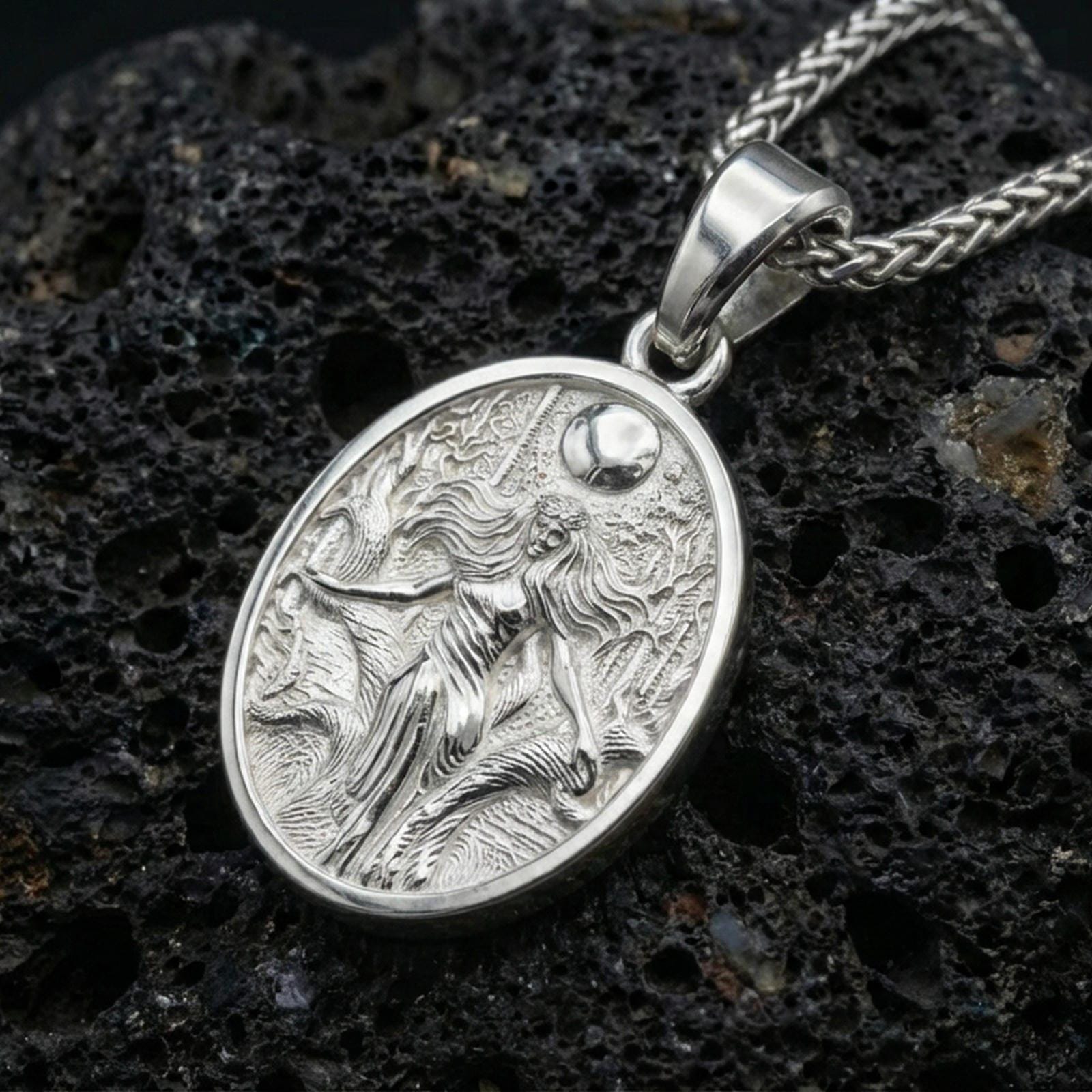 Polished silver Hela necklace pendant on volcanic rock, crisp engraved scene and textured background, close-up lighting