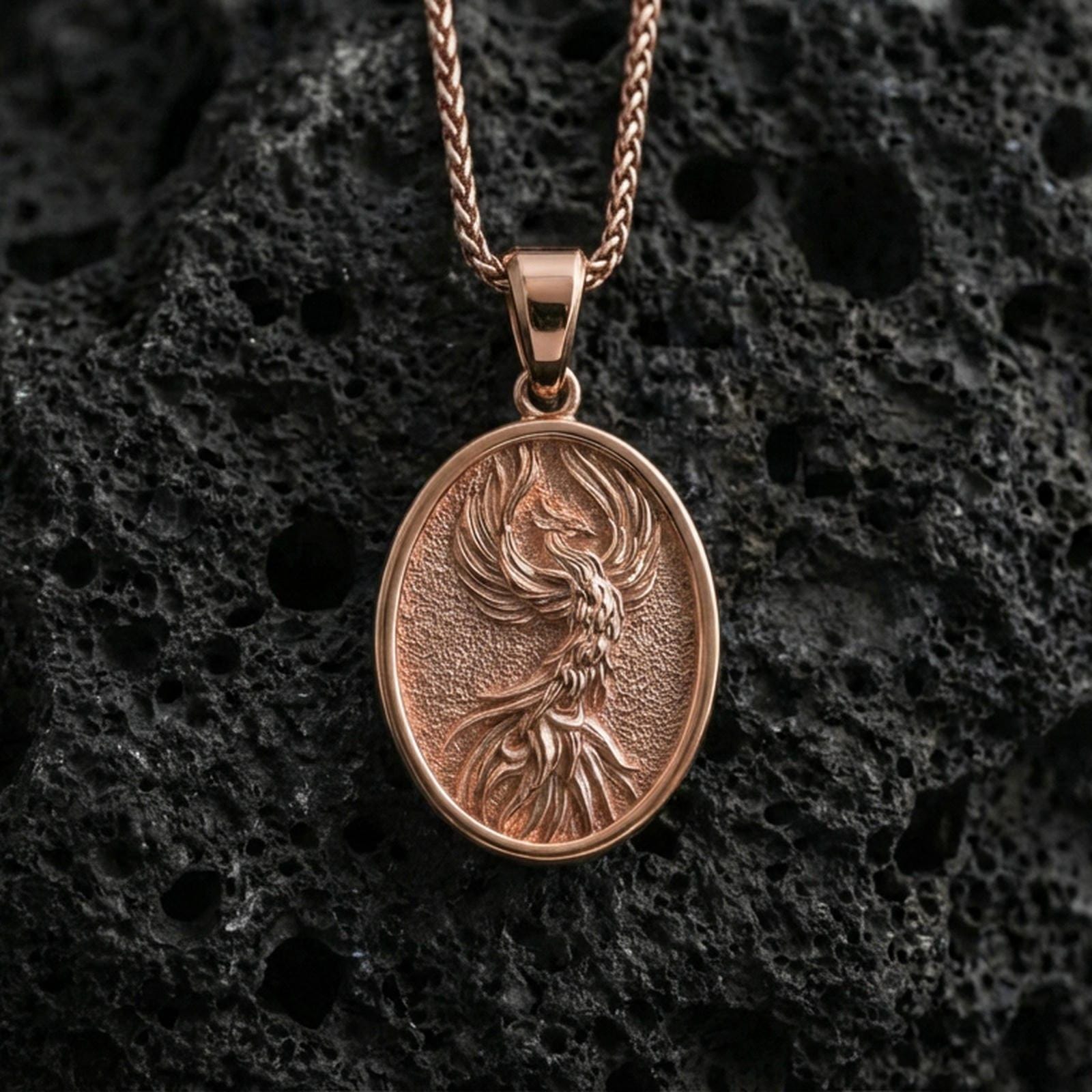 Rose gold plated phoenix medallion pendant on volcanic rock, textured lava stone background, detailed feather engraving