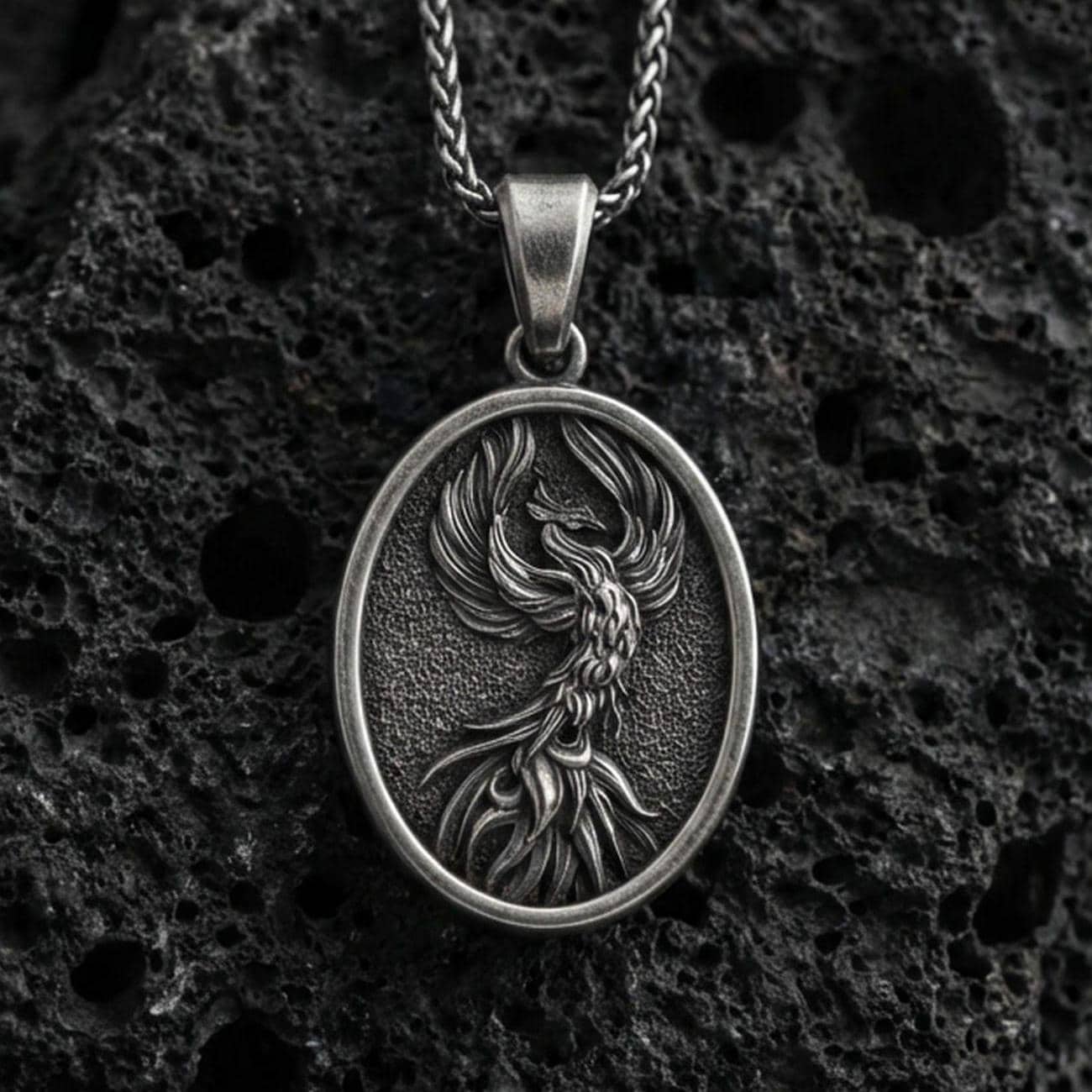 Oxidized sterling silver phoenix bird pendant on volcanic rock, rebirth symbol medallion with detailed feathers, macro shot
