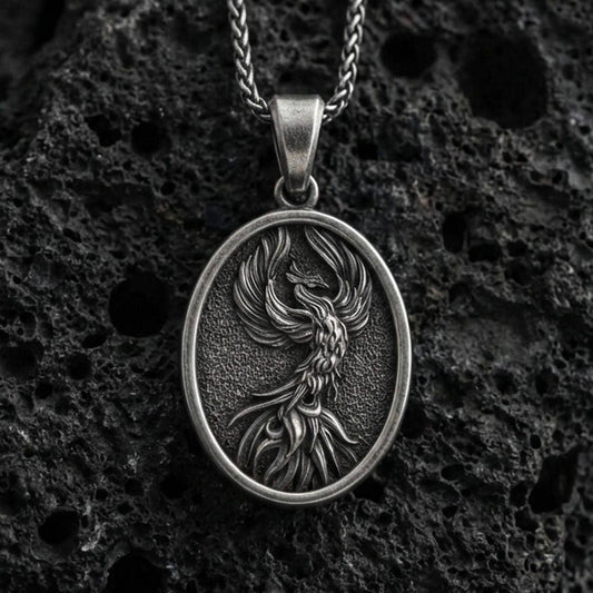 Oxidized sterling silver phoenix bird pendant on volcanic rock, rebirth symbol medallion with detailed feathers, macro shot