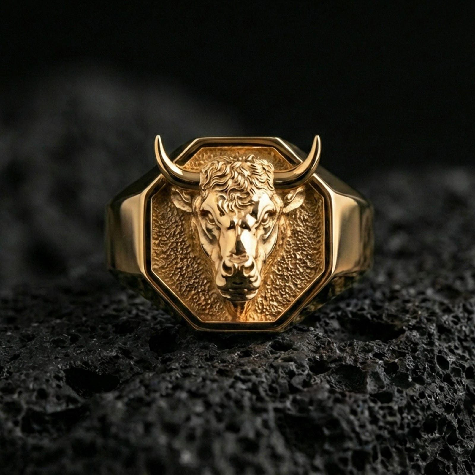 Gold plated bull head signet ring on volcanic rock, premium studio scene, powerful animal motif with sharp relief detail