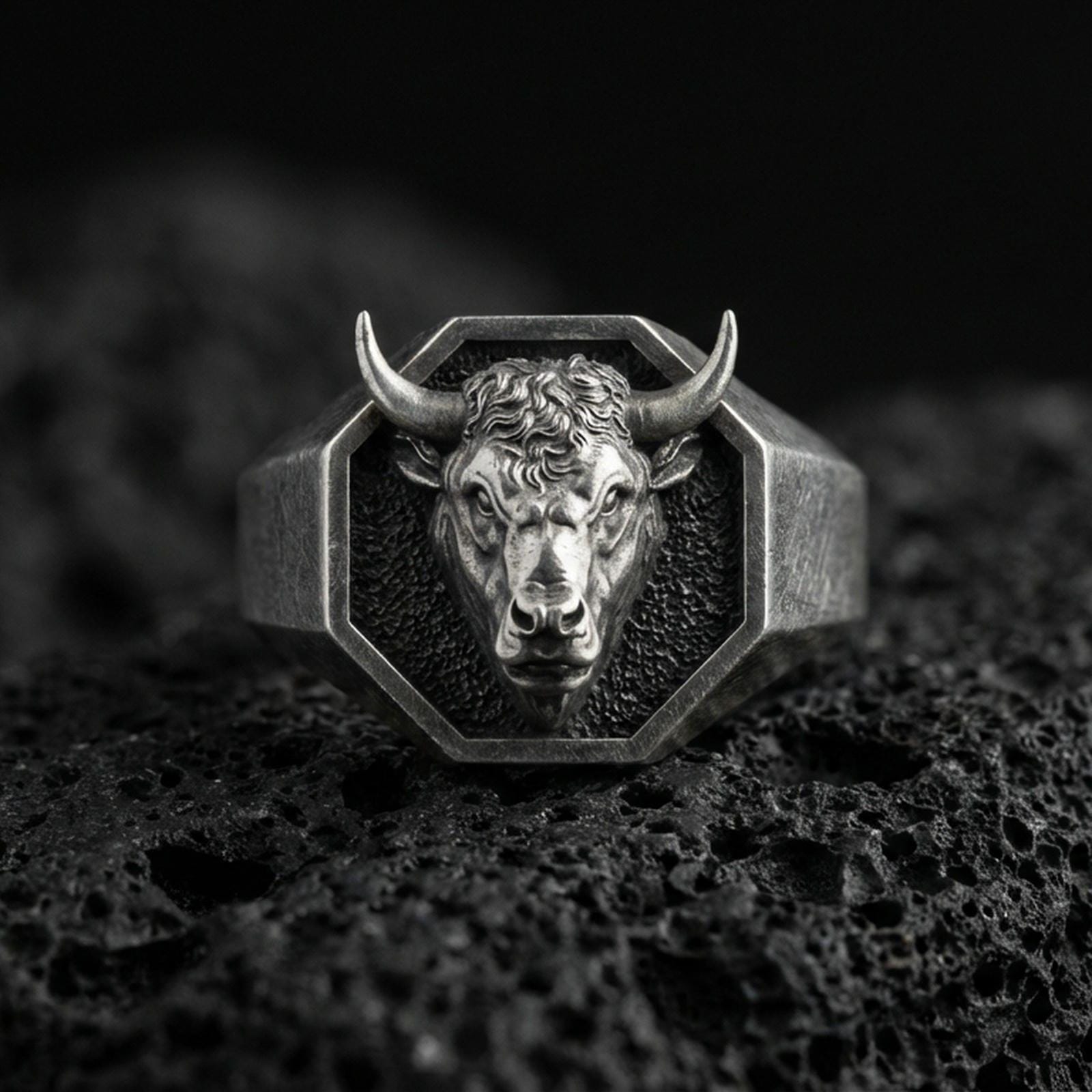 Oxidized sterling silver bull head signet ring on volcanic rock, octagonal face with high-relief horns, macro studio shot