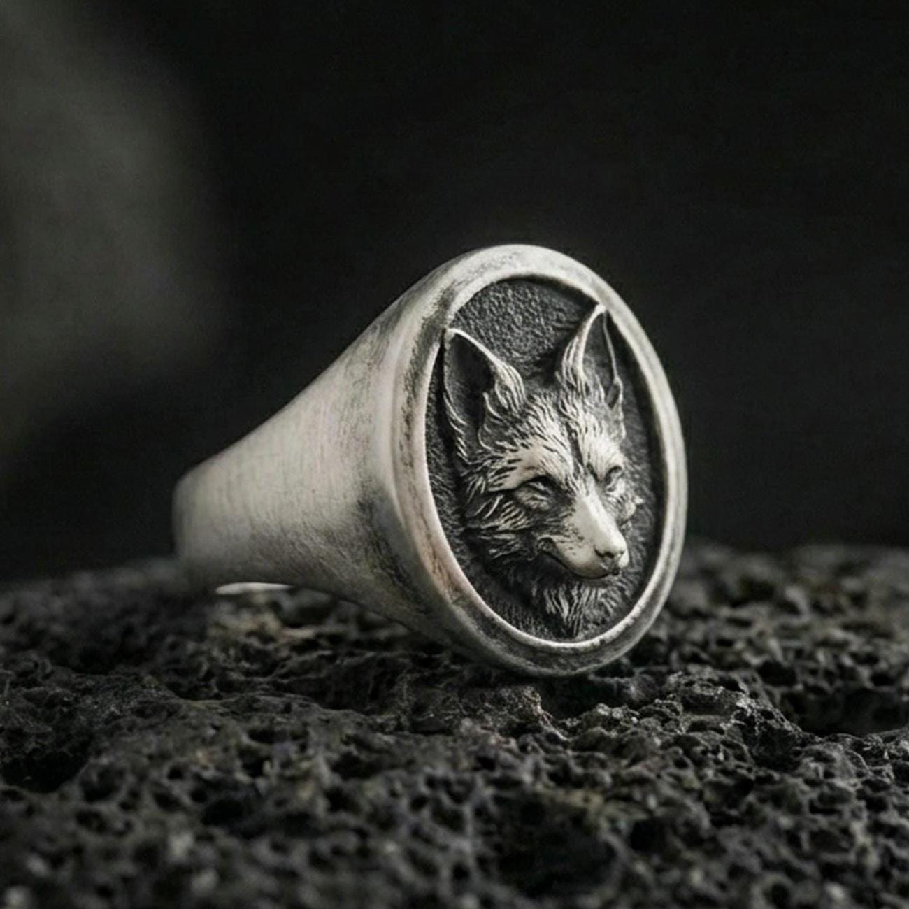 Oxidized sterling silver fox head signet ring on volcanic rock, round face with detailed fur texture, macro studio shot