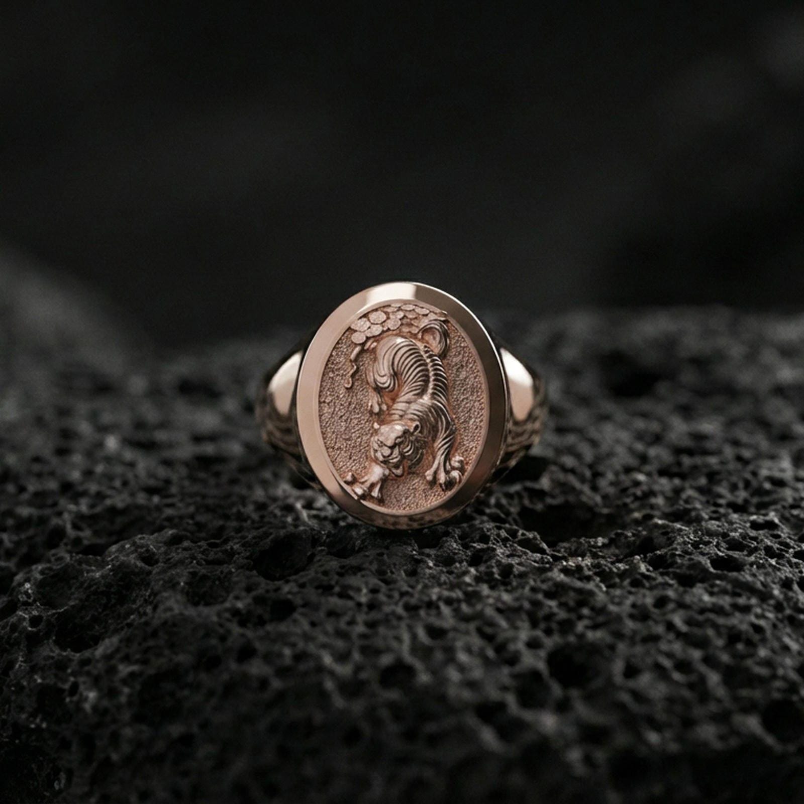Rose gold plated tiger signet ring on volcanic rock, textured lava stone background, detailed prowling pose engraving