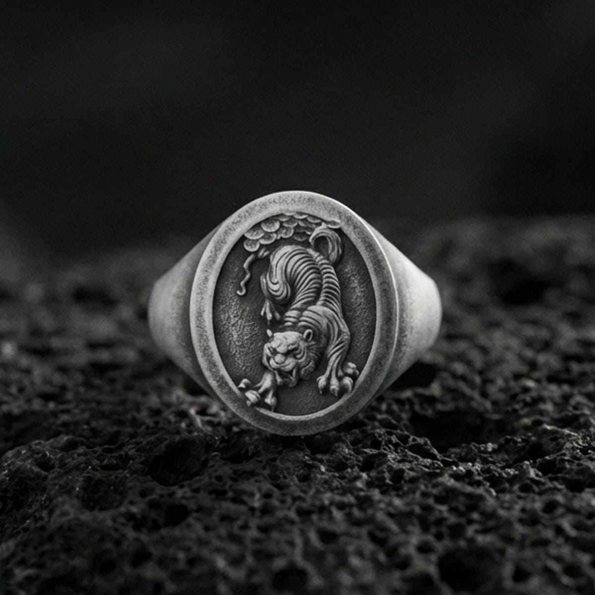 Oxidized sterling silver Asian tiger signet ring on volcanic rock, prowling tiger relief with textured background, macro shot