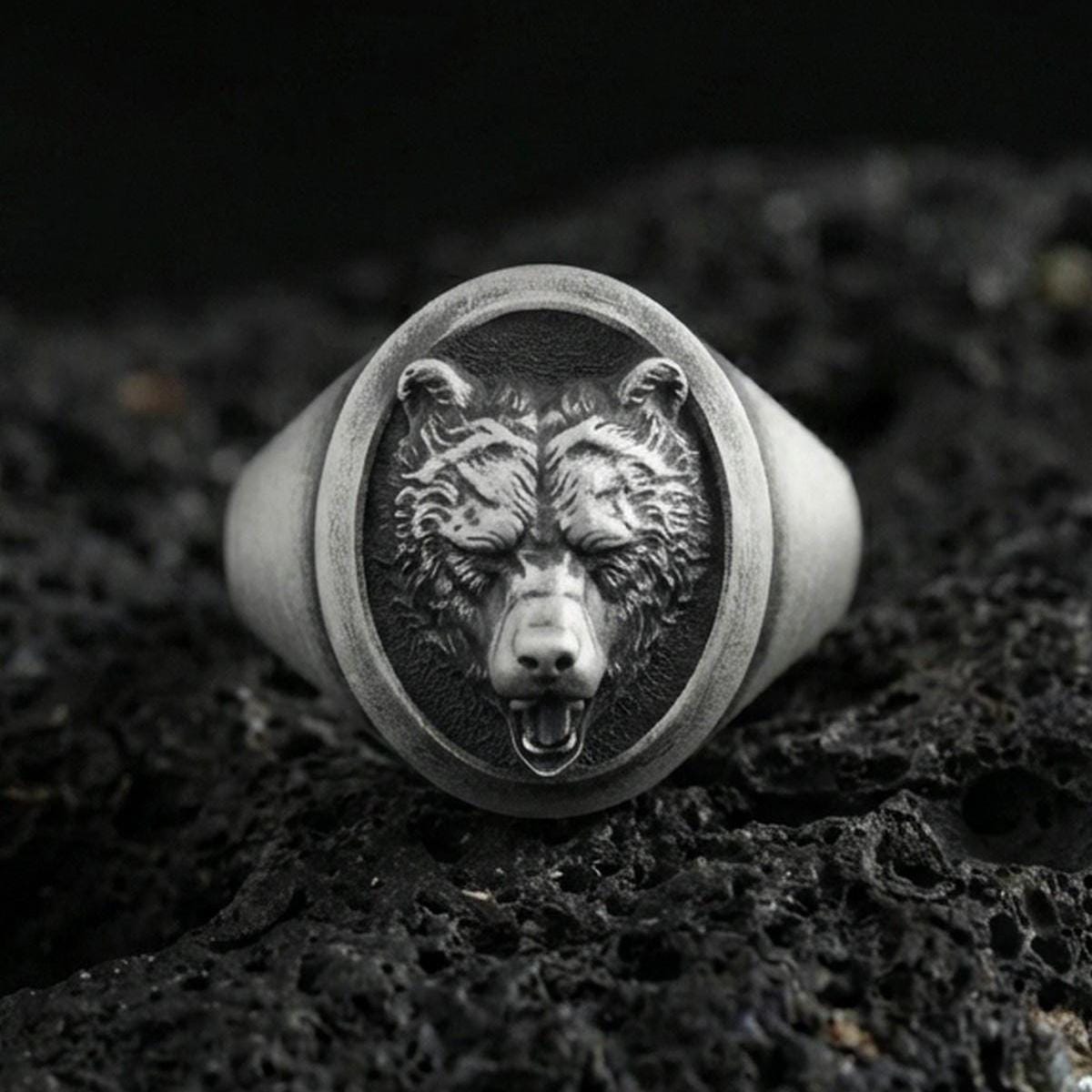 Oxidized sterling silver bear head signet ring on volcanic rock, detailed fur texture and open-mouth relief, macro studio shot