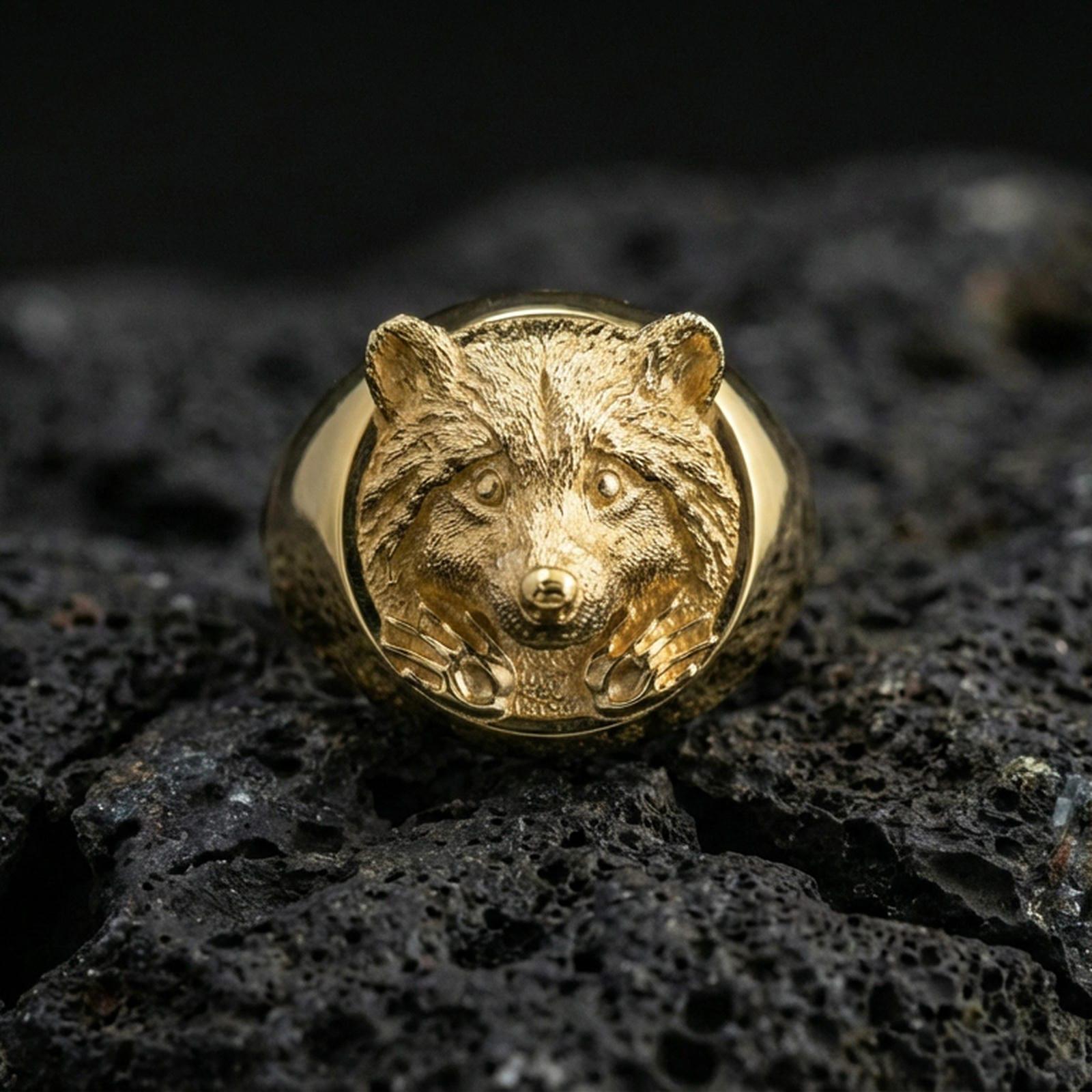Gold plated raccoon head signet ring on volcanic rock, premium studio scene, nature-inspired animal motif with bold relief