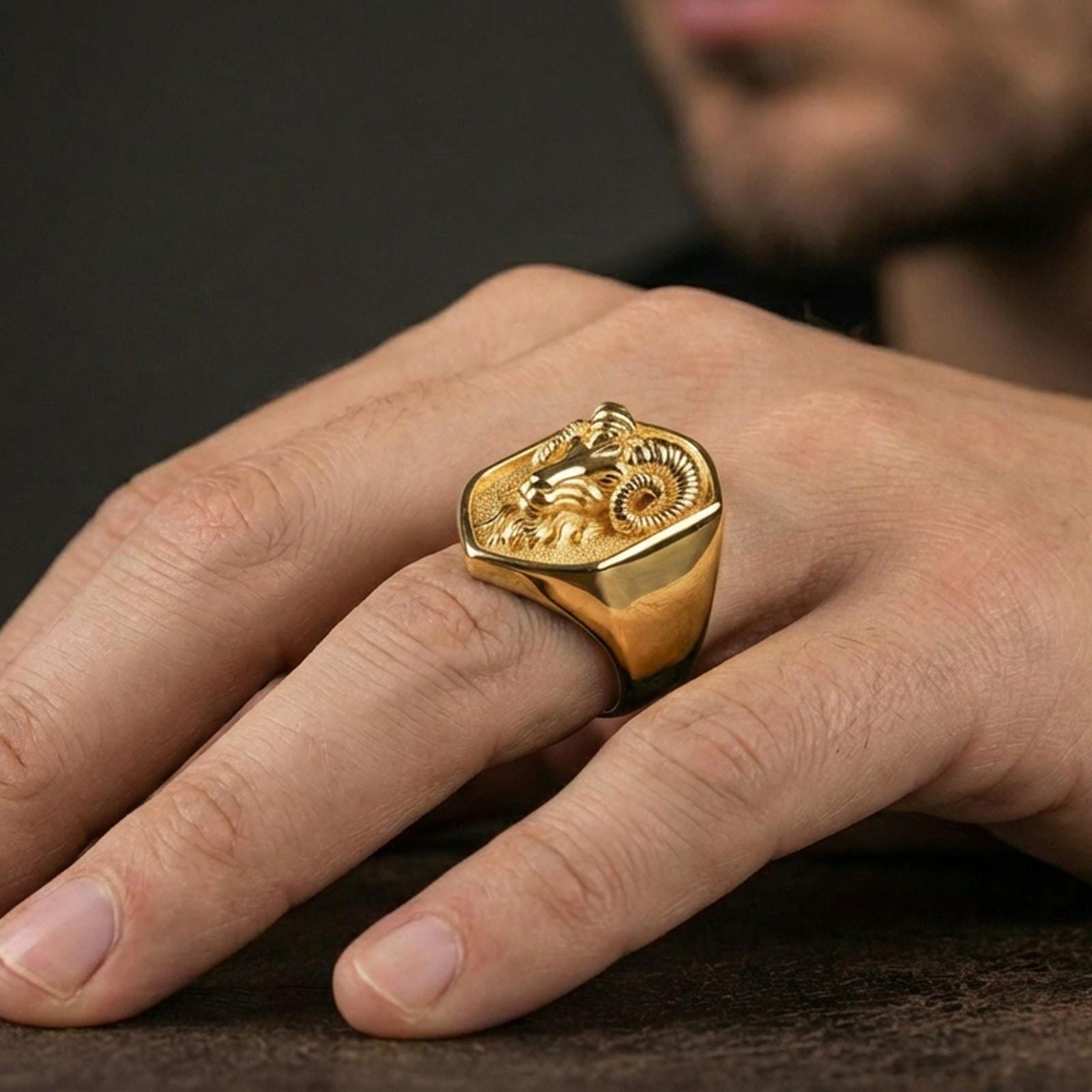 Gold plated ram head signet ring worn on finger, premium lifestyle framing, statement animal signet ring focal detail