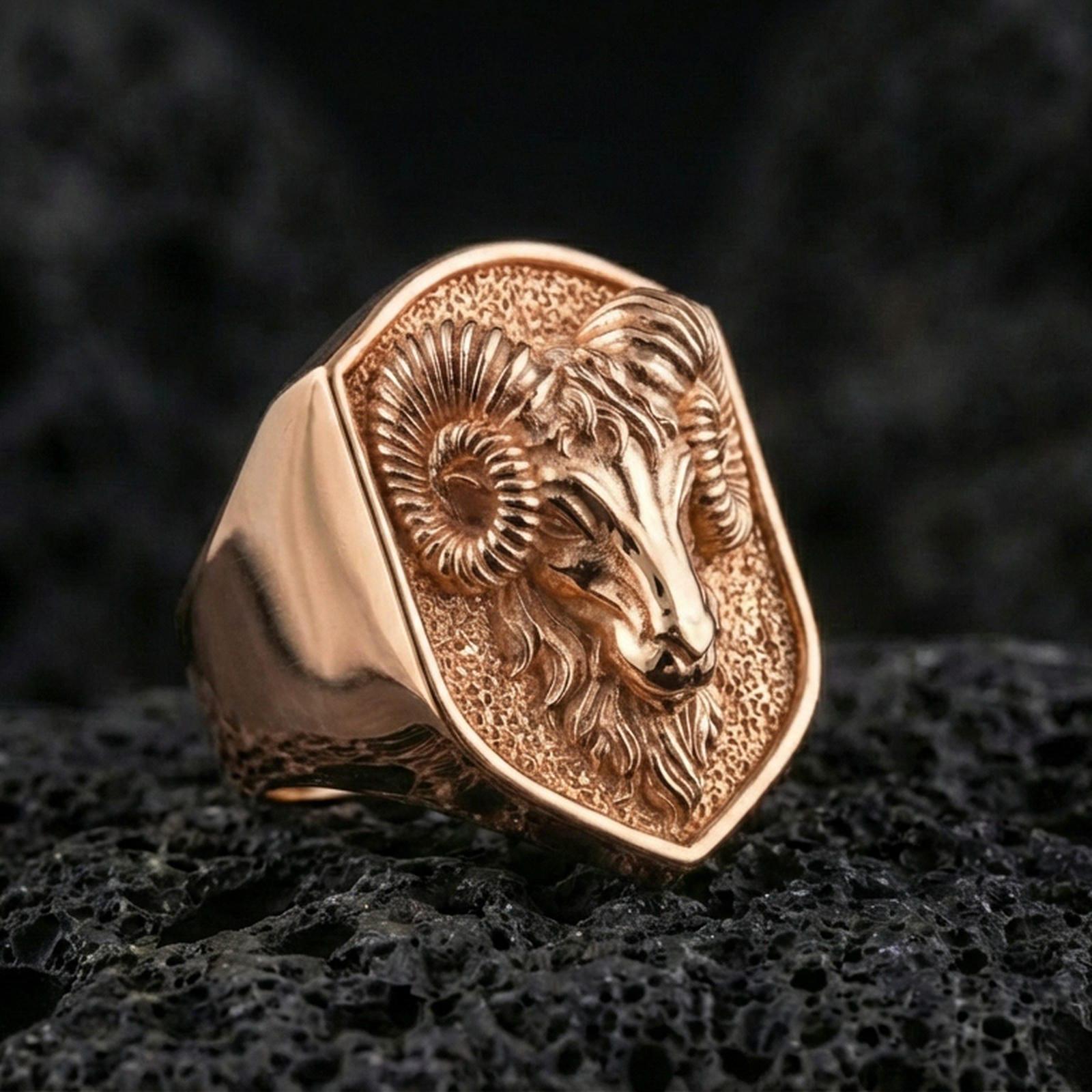 Rose gold plated ram head signet ring on volcanic rock, detailed ram head relief with coiled horns, luxury product close-up