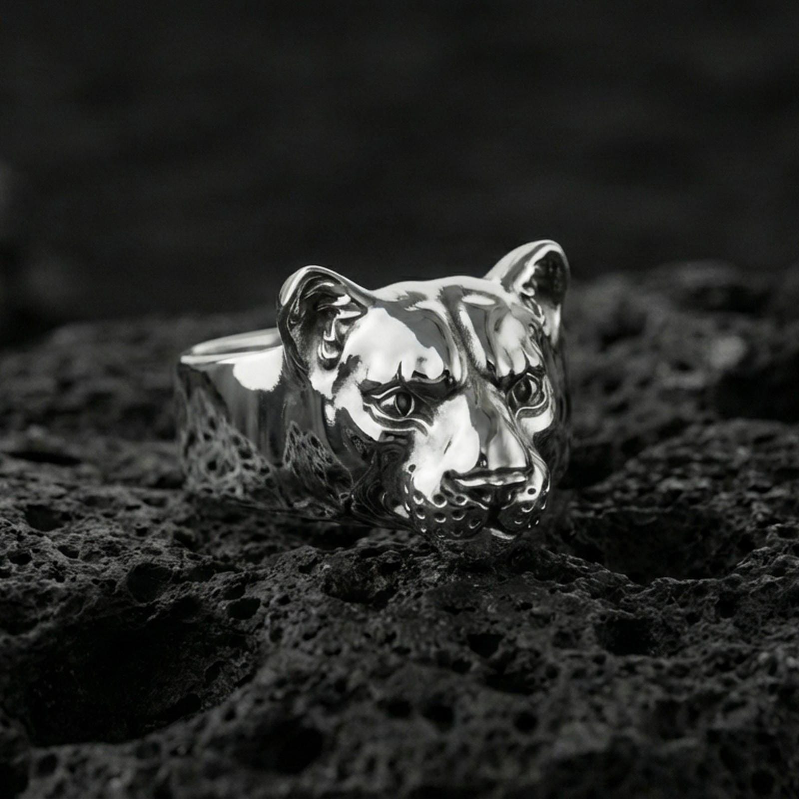 Polished silver puma head ring on volcanic rock, glossy feline muzzle and sculpted ear contours, studio close-up