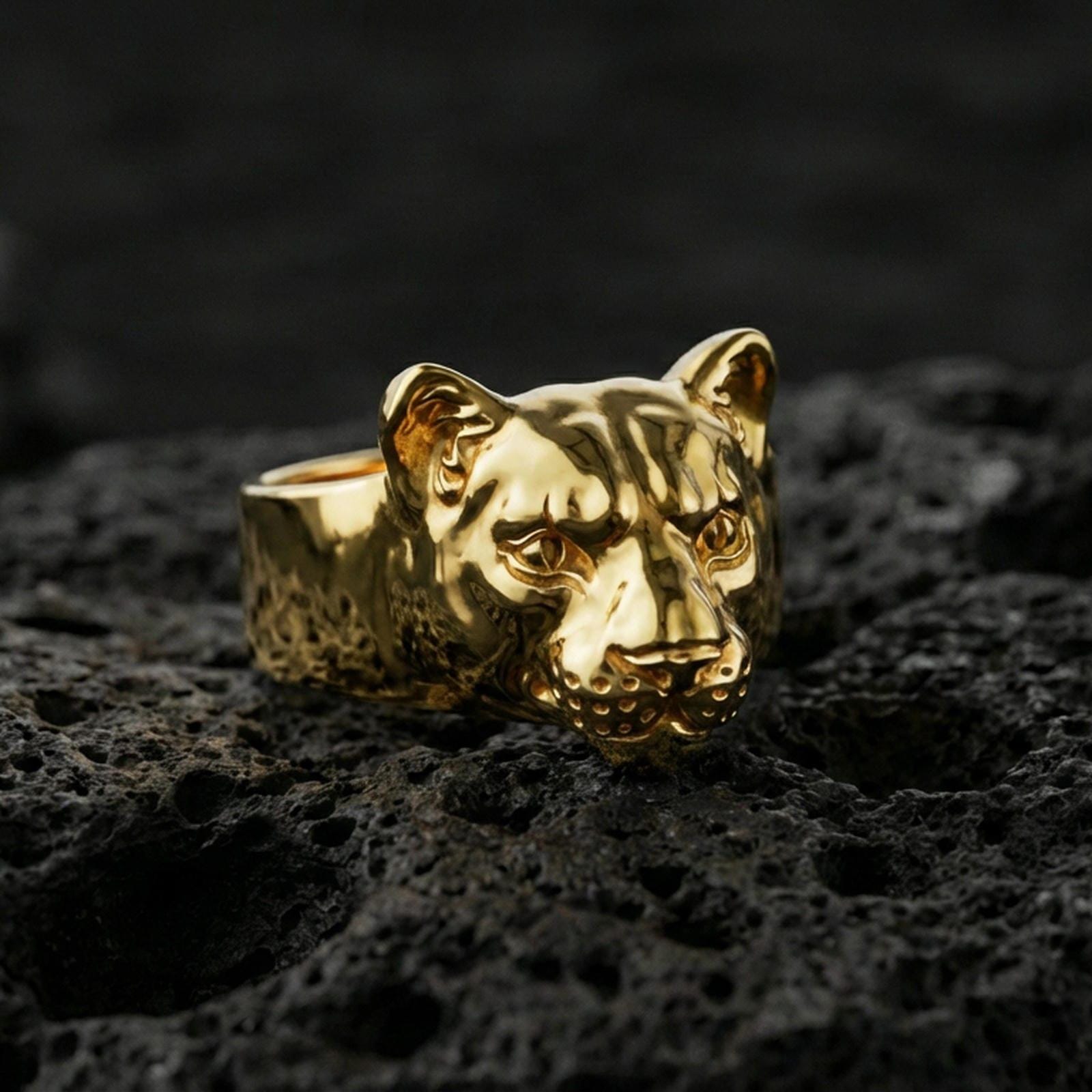 Gold plated puma head ring on volcanic rock, sleek wild cat head design with defined whisker dots, premium macro lighting